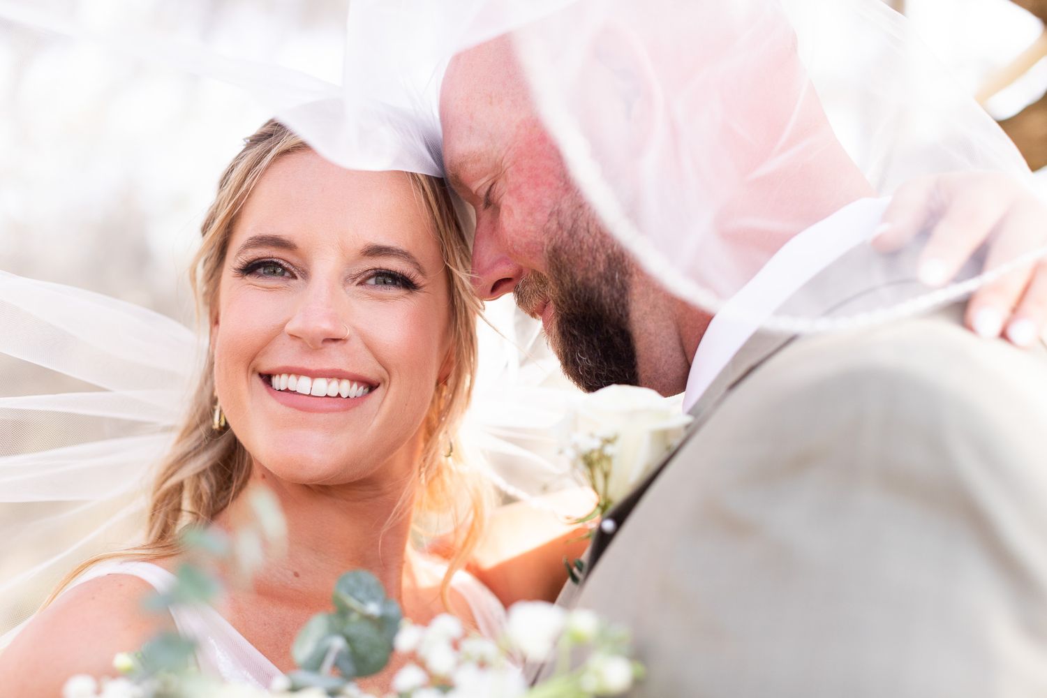 Close-up wedding portrait showing joyful expressions and white floral details.