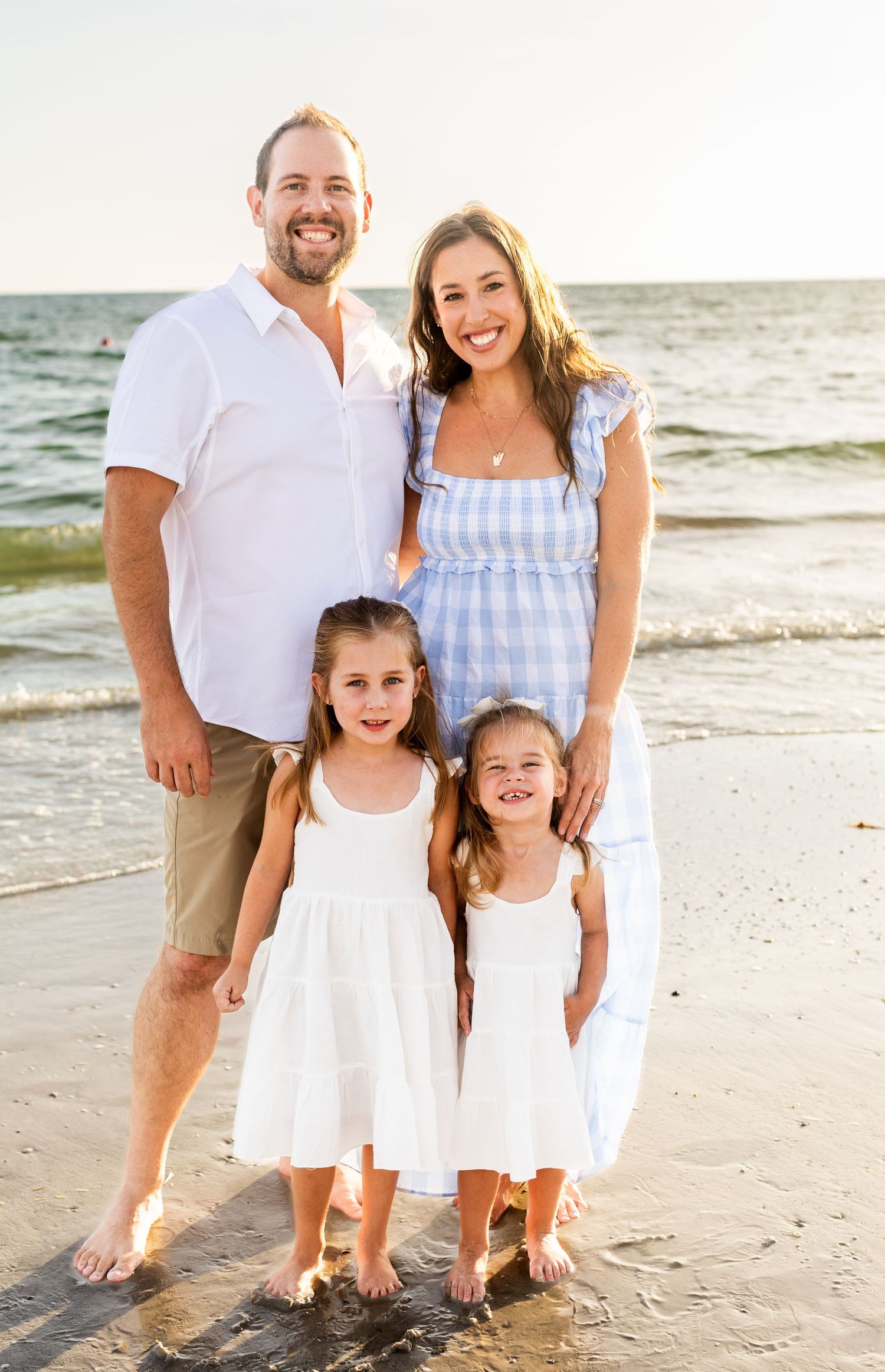 Family poses together on the beach wearing coordinated white and blue outfits.