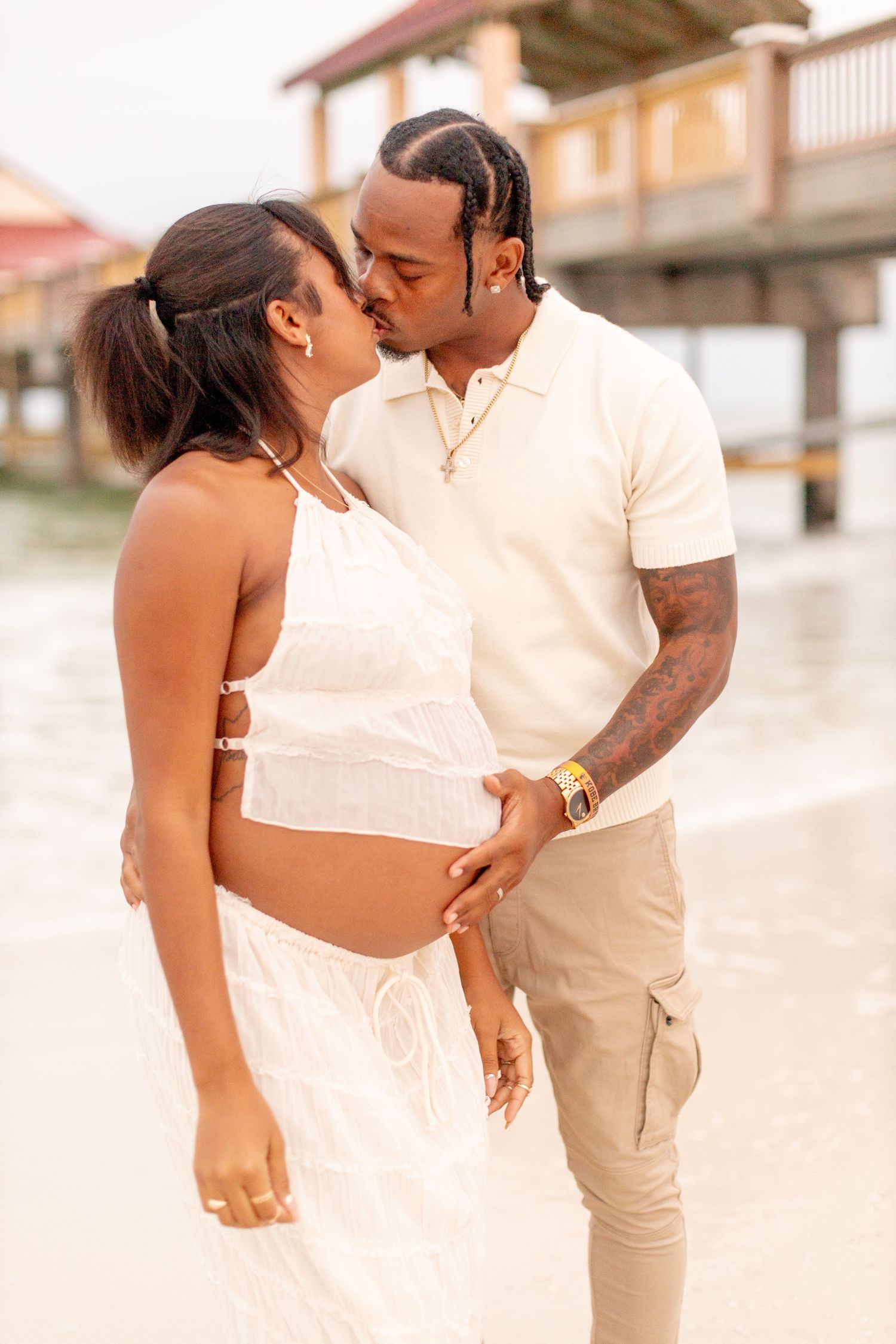 A romantic couple in white and beige outfits shares an intimate moment on the beach.
