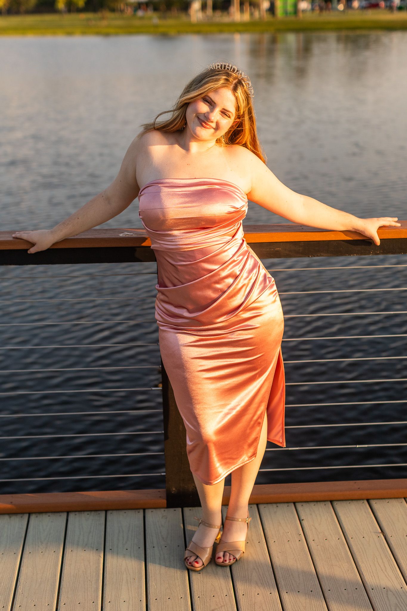 Elegant pink satin dress photographed during golden hour on waterfront boardwalk.