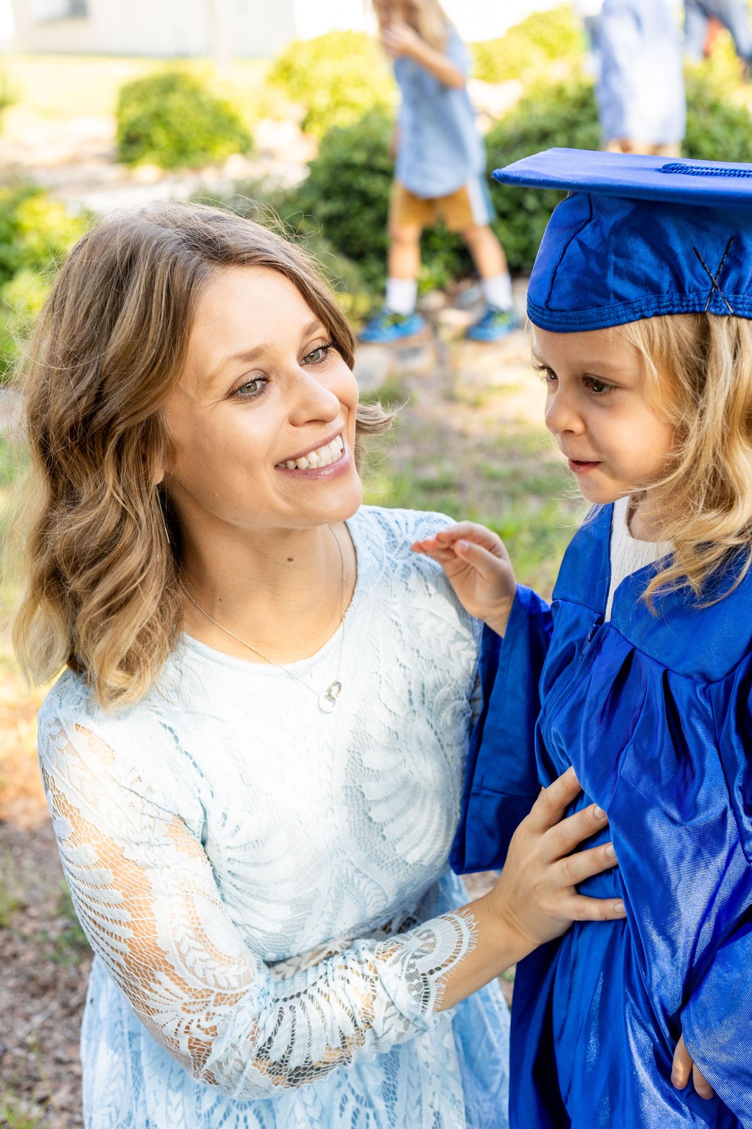 A touching graduation moment outdoors with a graduate in blue regalia and companion in white lace.
