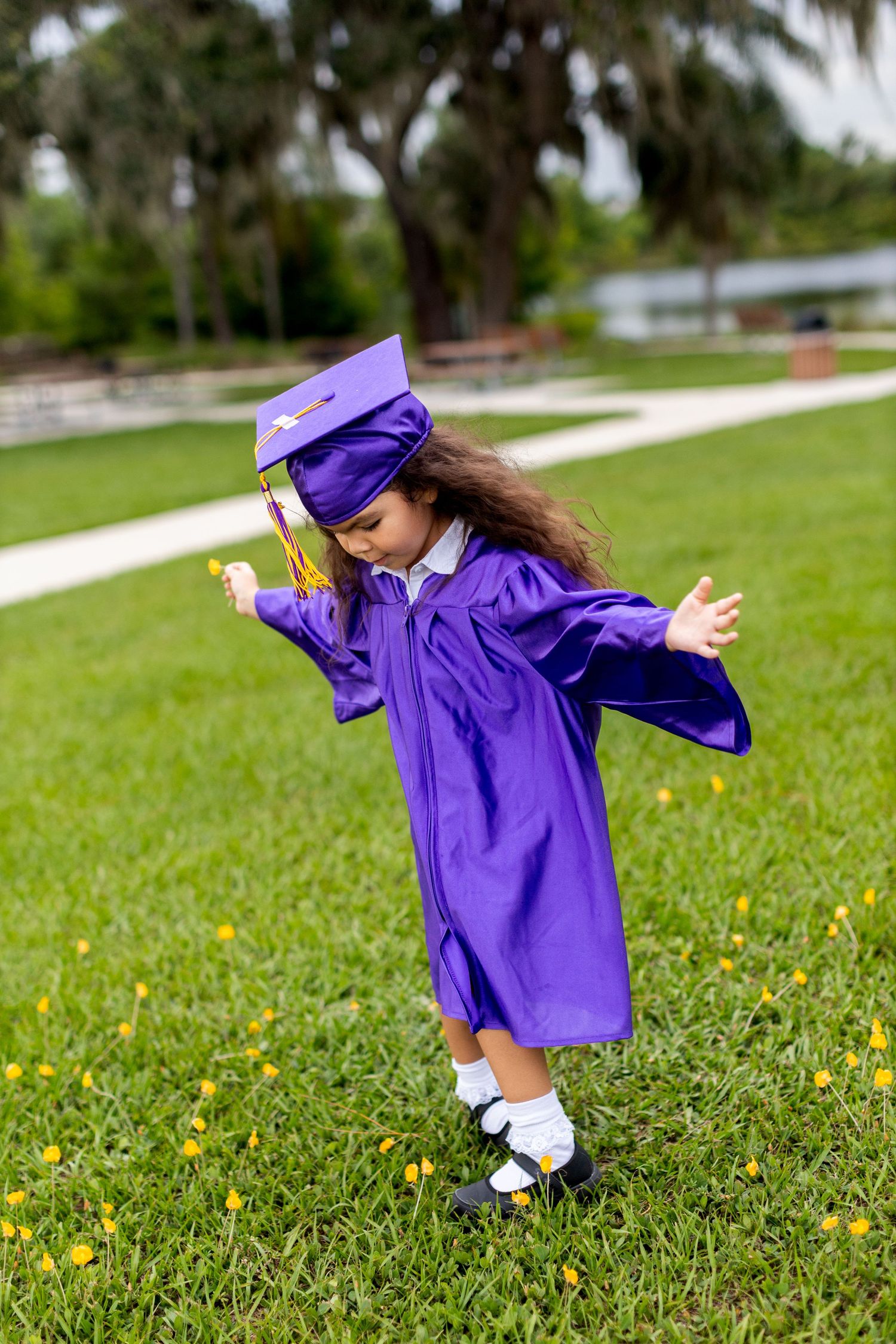 Playful poses of a graduate in purple cap and gown twirling on grass with yellow flowers.