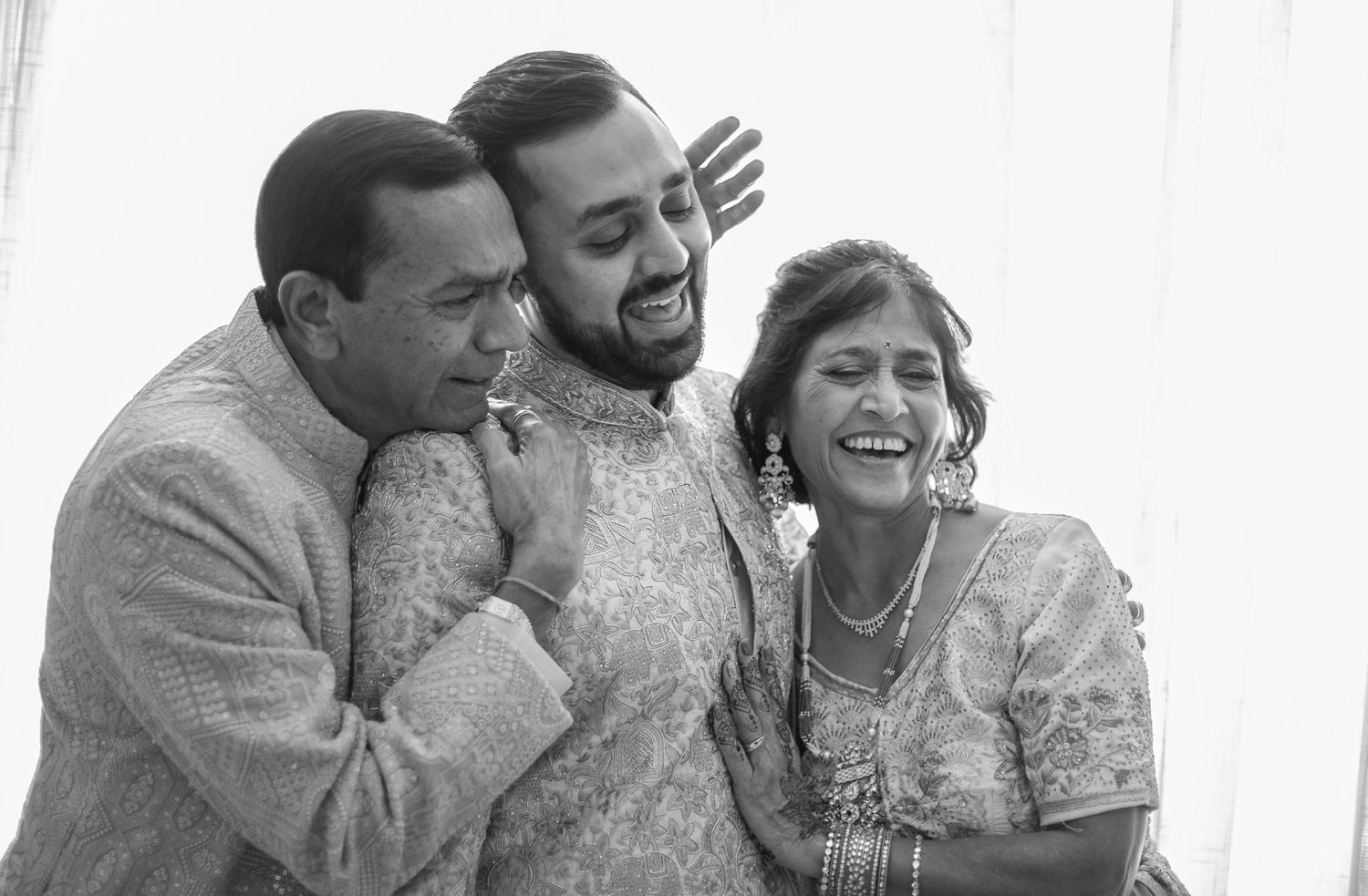 Three people share a candid black and white moment during a wedding celebration.