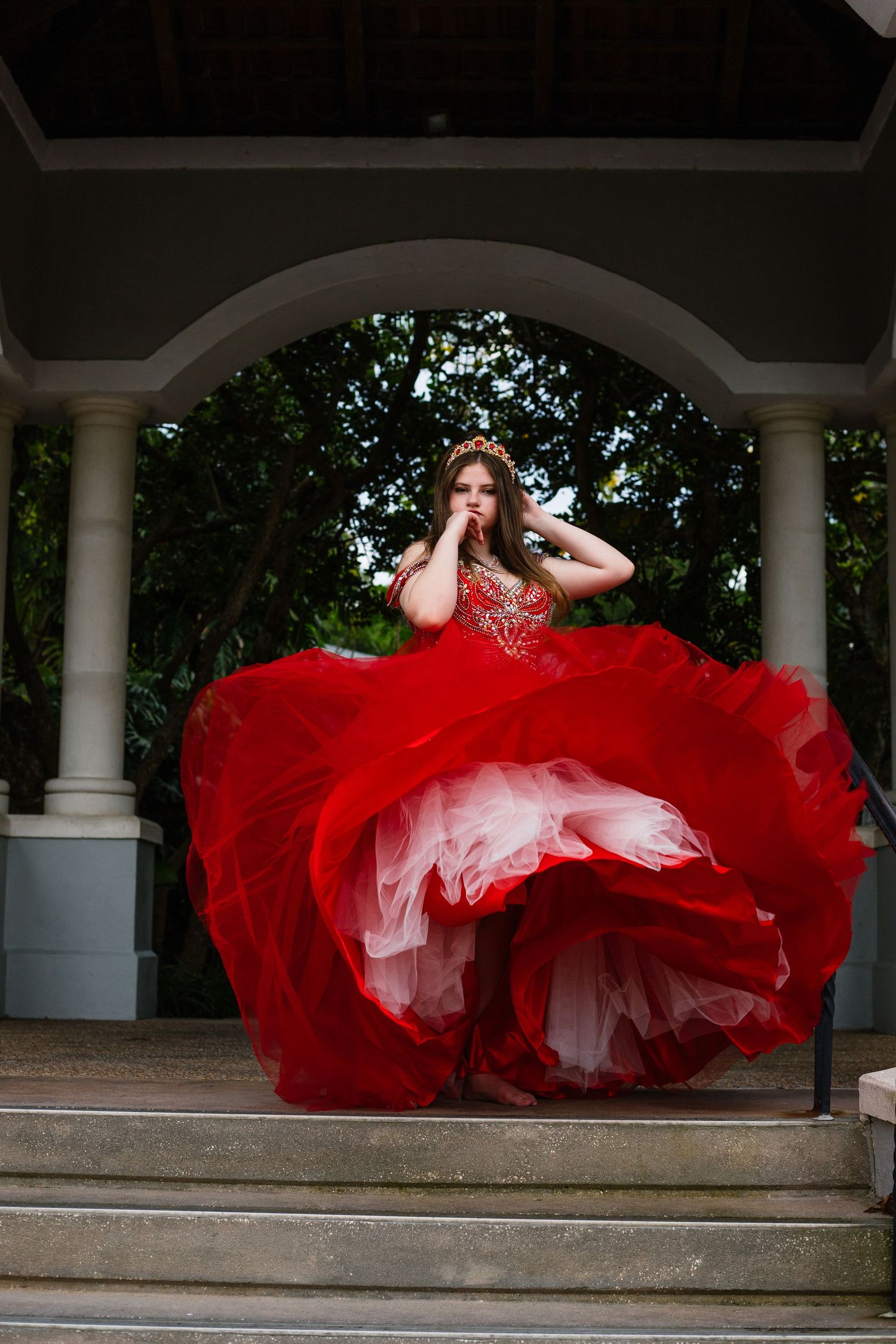 Dramatic red ballgown dress flowing in motion across stone steps with white columns.