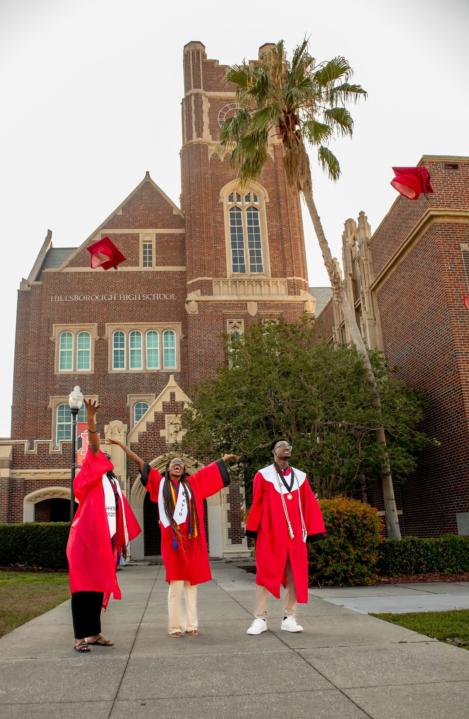 People in red graduation robes strike fun poses outside historic brick building.