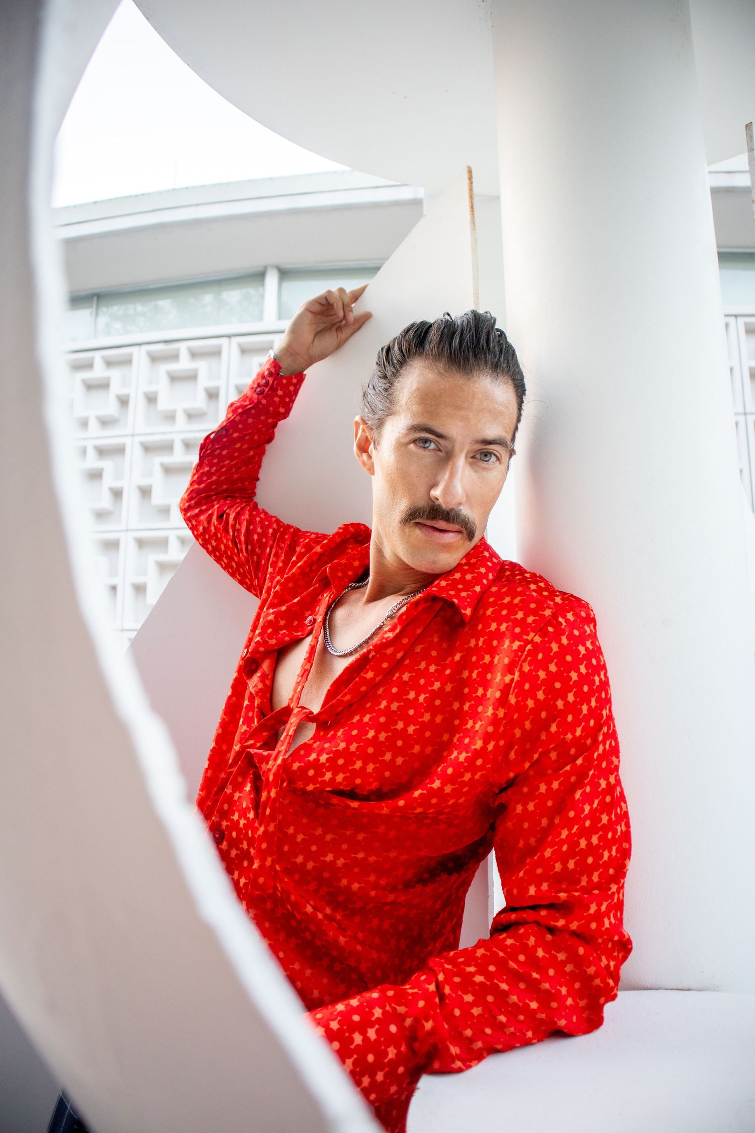 Modern fashion portrait in white architectural space wearing vibrant red patterned shirt.
