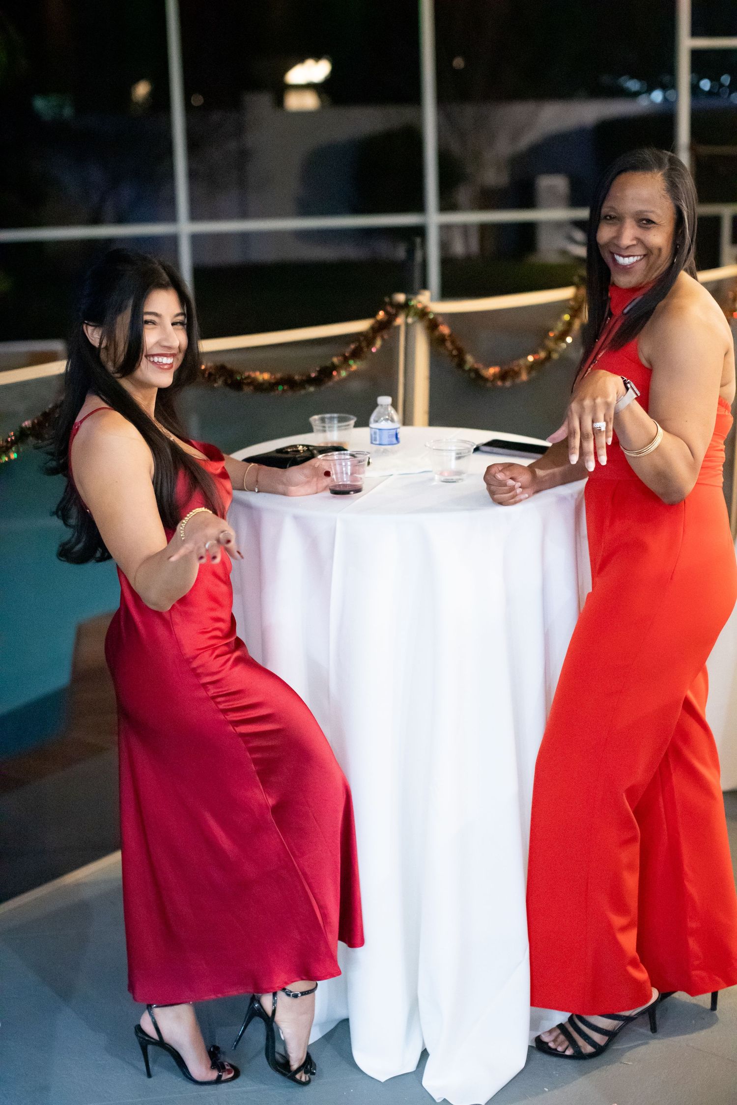 Women in red dresses pose around a white table at an elegant event.