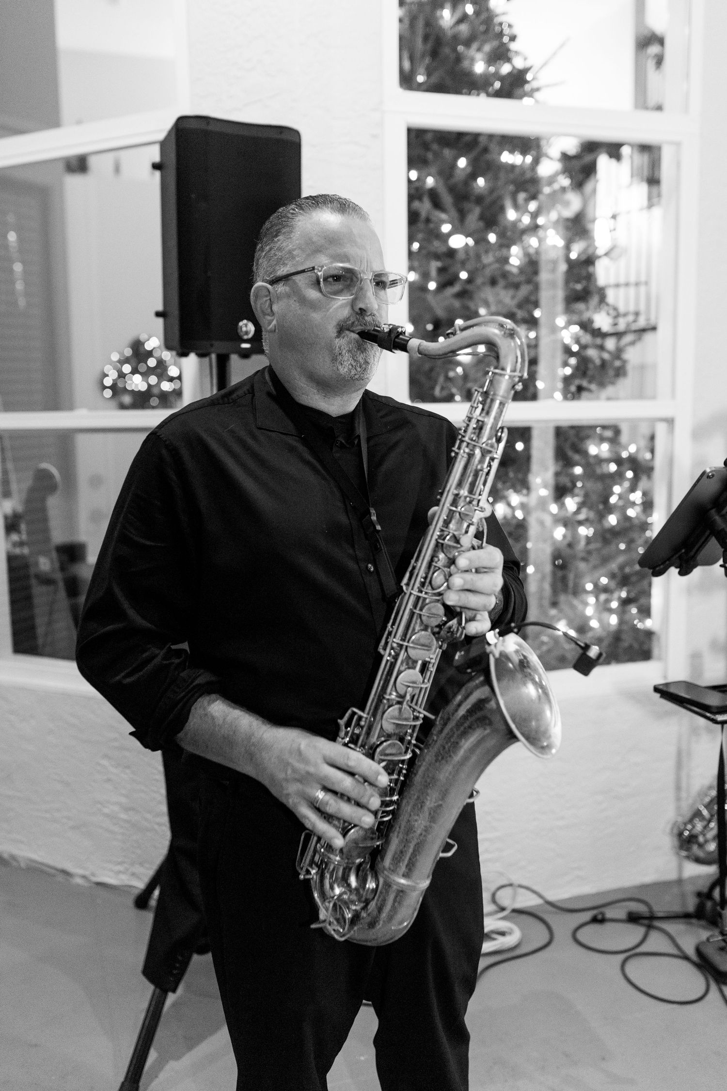 A saxophone player performs in black attire against a white backdrop with holiday decorations.