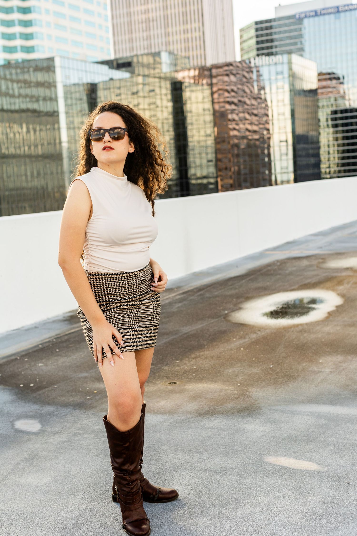 Street fashion photography with plaid mini skirt and boots against modern city skyline.
