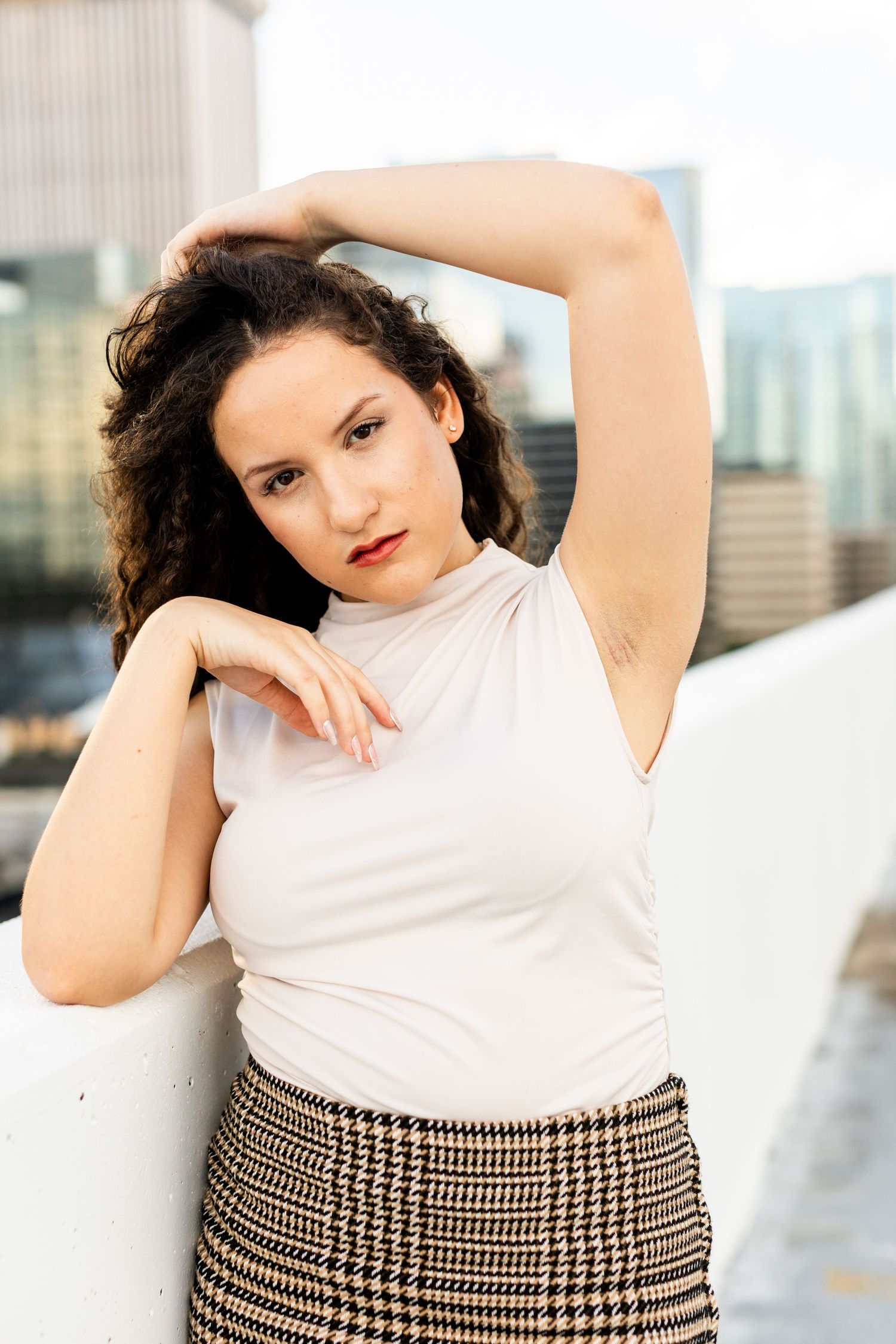 Stylish pose against urban backdrop in white sleeveless top and plaid skirt.
