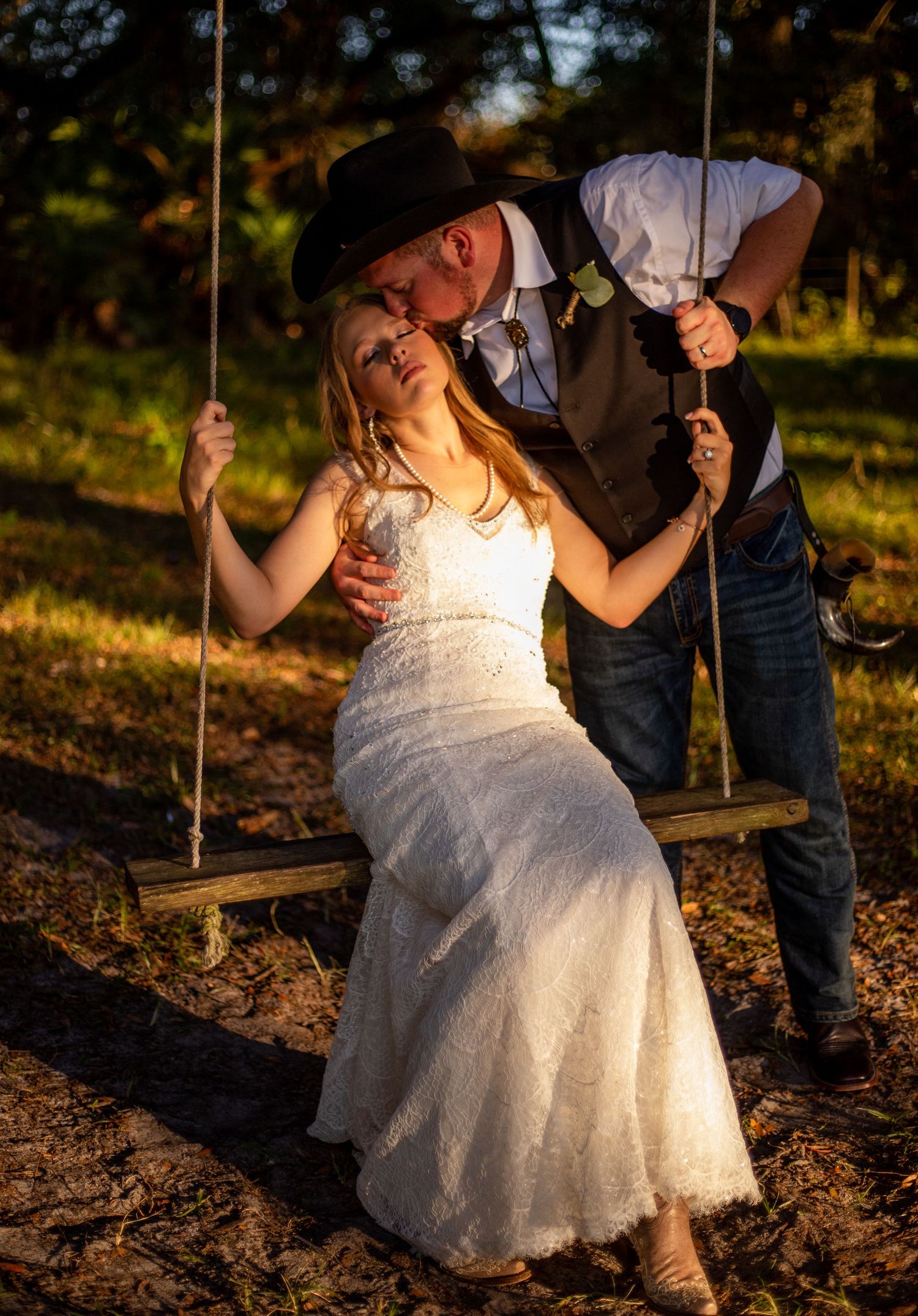Bride on rustic wooden swing captured in golden sunset light during wedding portraits.