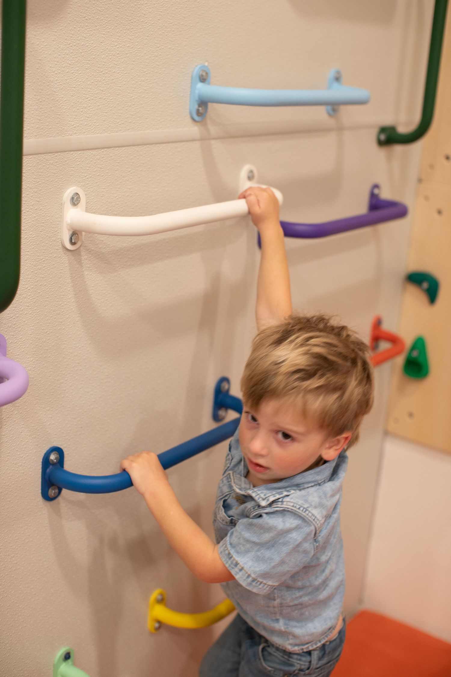 Child reaches for colorful handholds on indoor climbing wall.