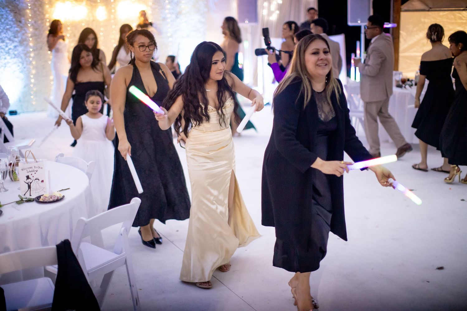 Wedding guests dancing together in formal attire on a white dance floor with ambient lighting.