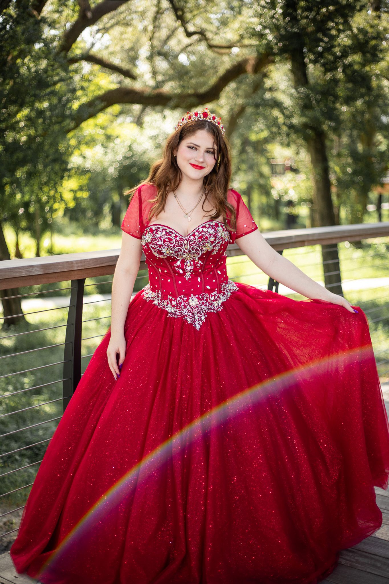 Elegant red ballgown with beaded bodice and full tulle skirt photographed on a wooden deck in natural light.
