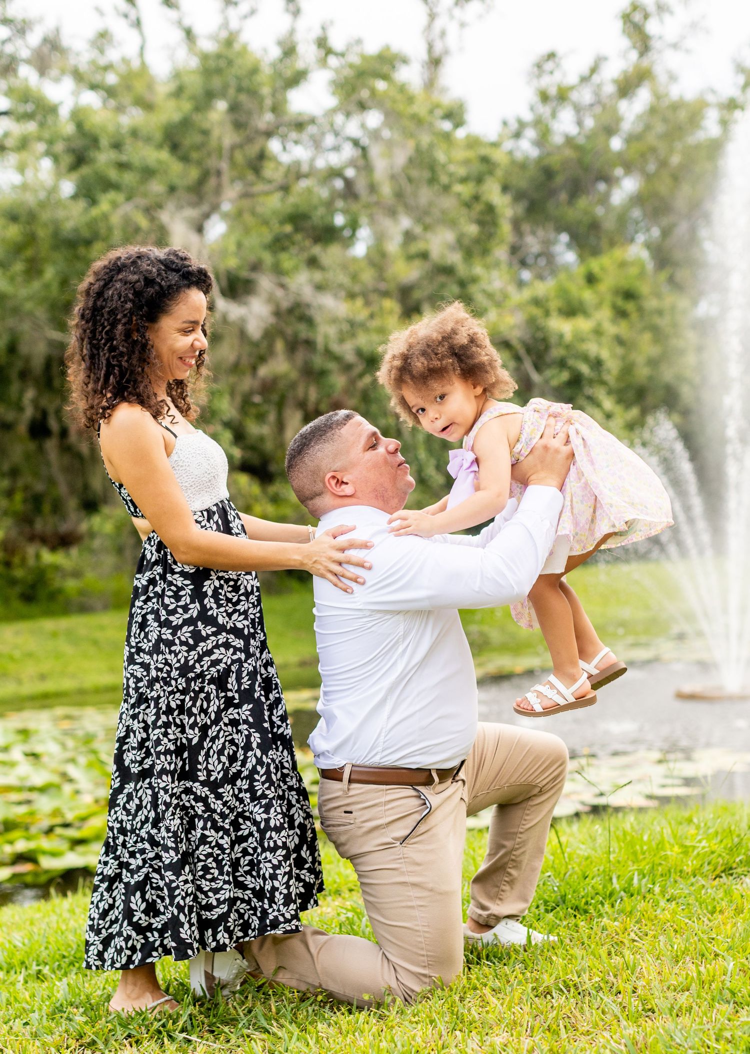 Playful family moment captured on green grass with fountain spray in background.