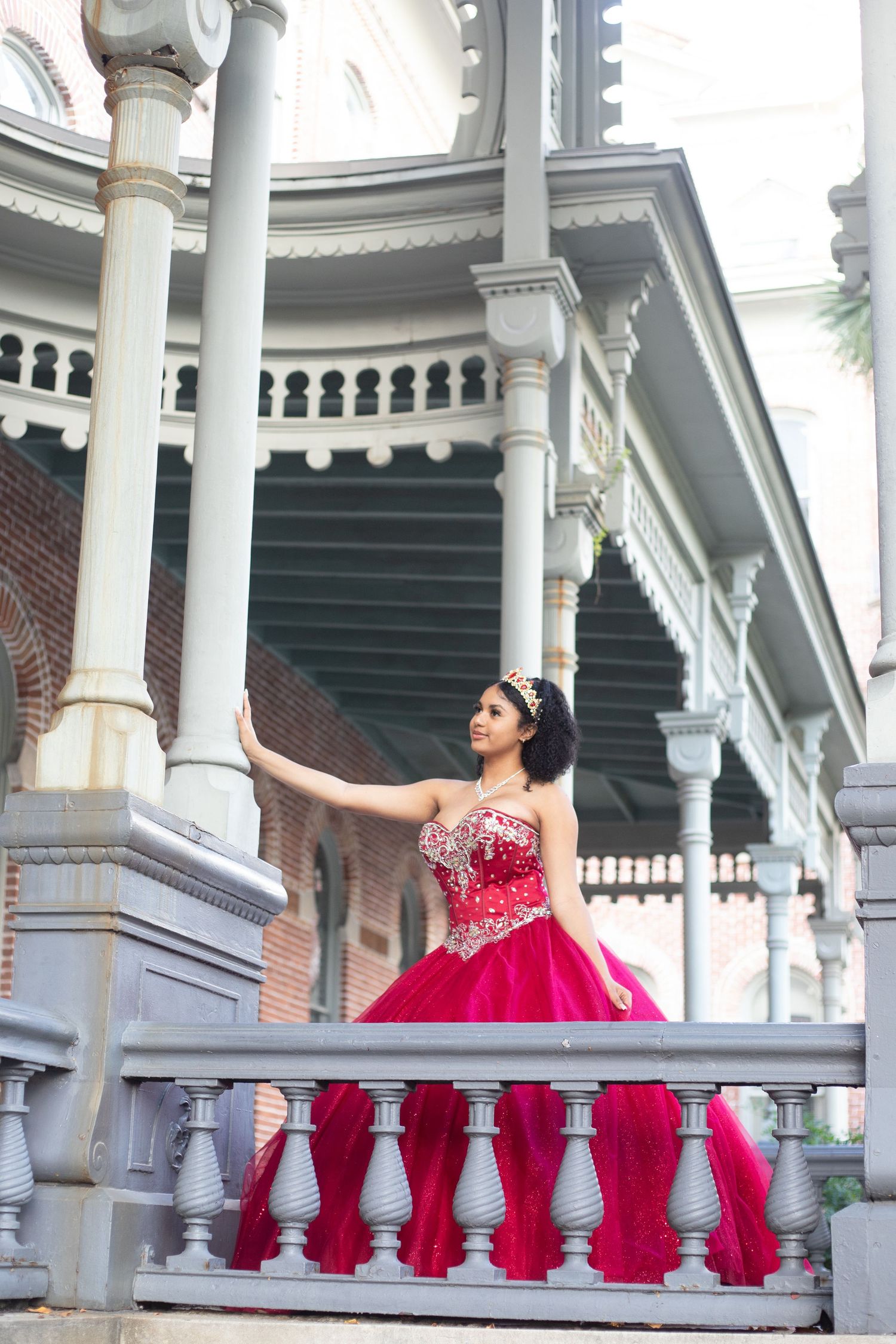 Red formal dress displayed against classic white colonial architecture and columns.