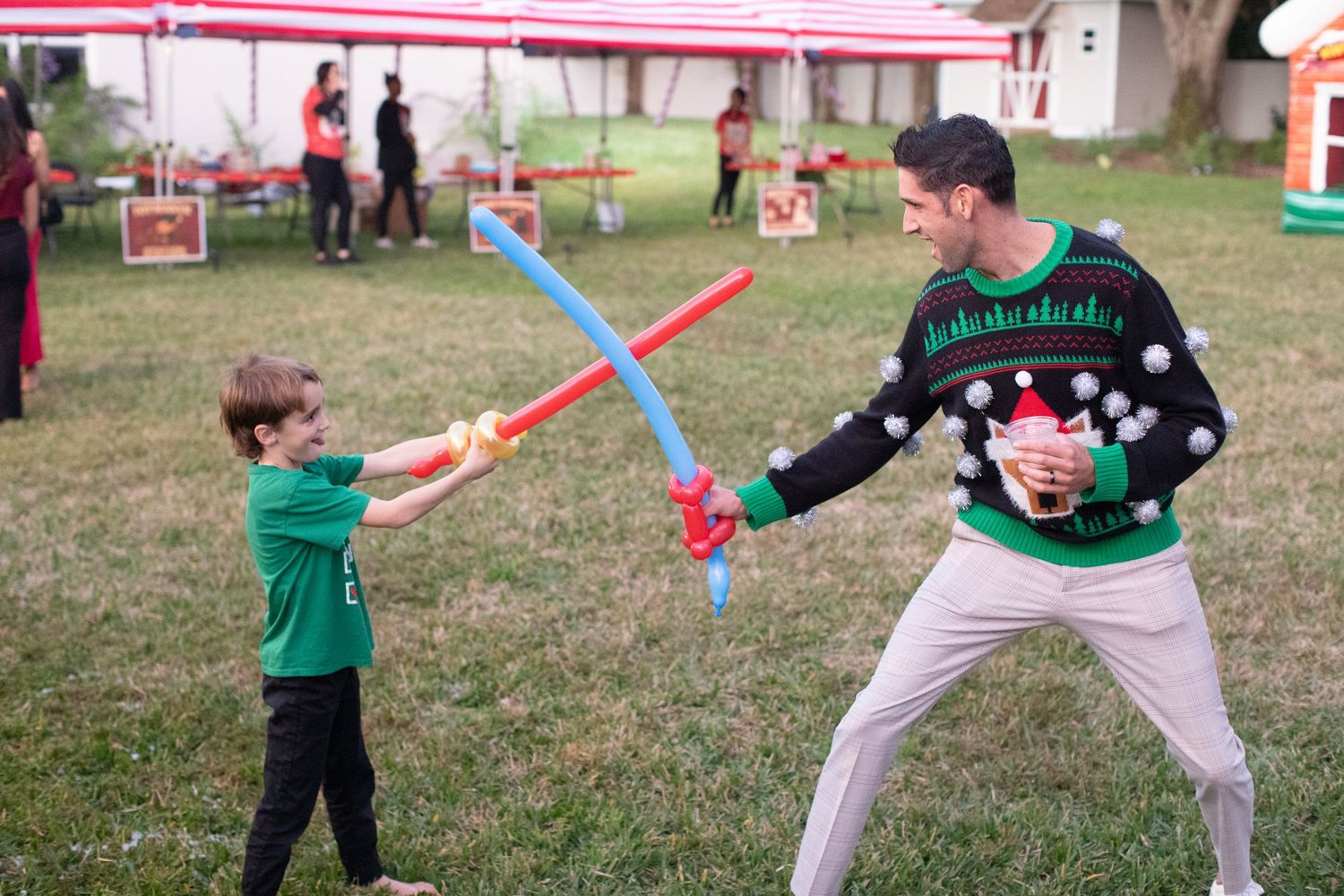 Children playing with colorful lightsabers in a grassy outdoor area.