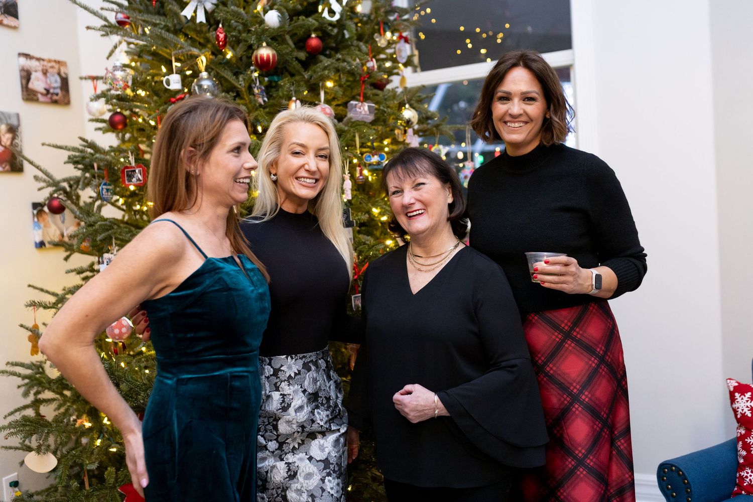 Four people gather for a photo in front of a decorated Christmas tree at a festive celebration.