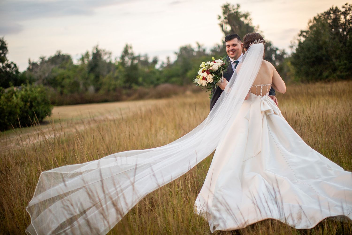 Bride's flowing white dress billows dramatically in the wind during sunset portraits.