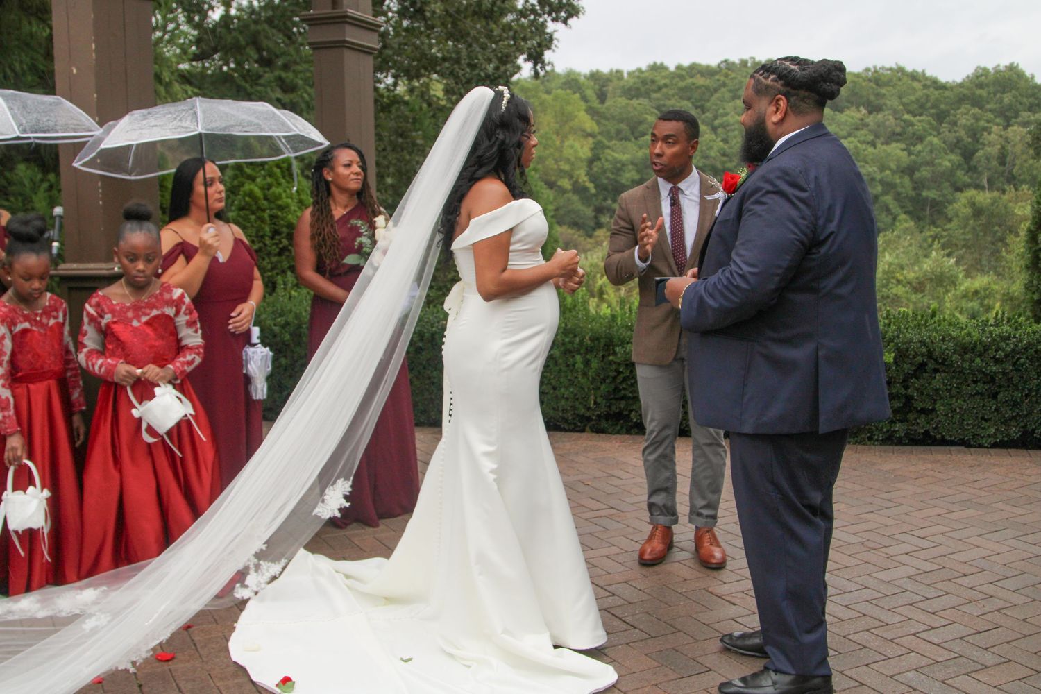 Wedding ceremony on brick patio with white gazebo and red rose petals scattered on ground.