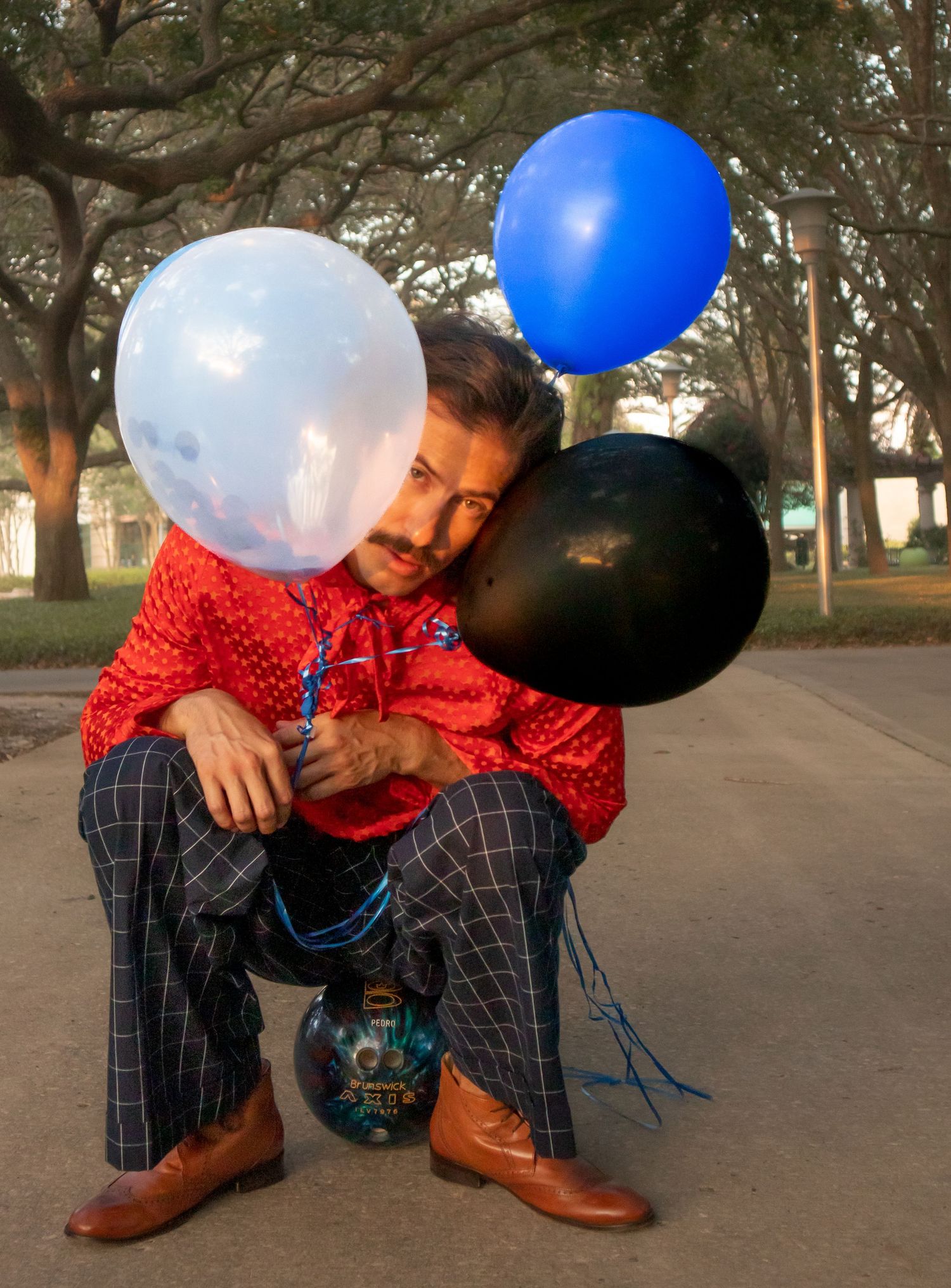 Playful pose with blue, white and black balloons in a park setting.