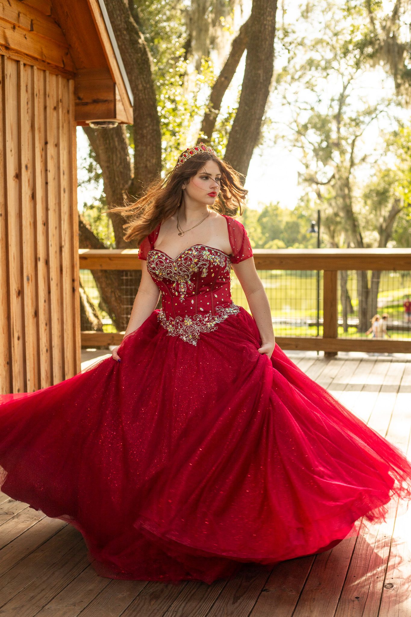 Flowing red ball gown with crystal embellishments photographed on wooden deck at sunset.