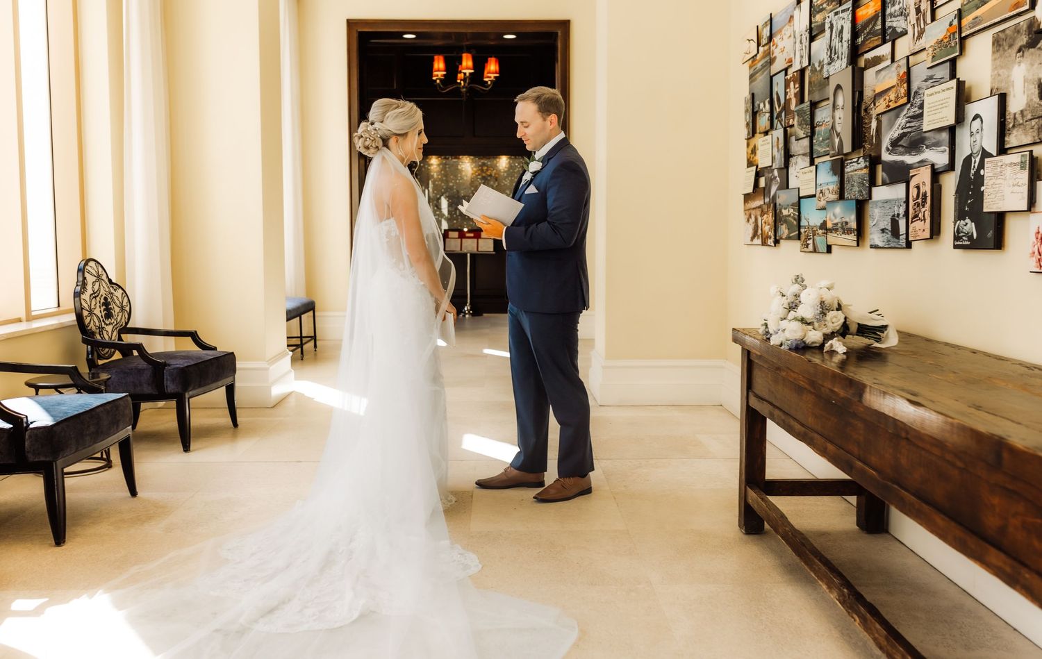 Bride and groom exchanging vows indoors at elegant wedding venue with white walls and photo gallery backdrop.