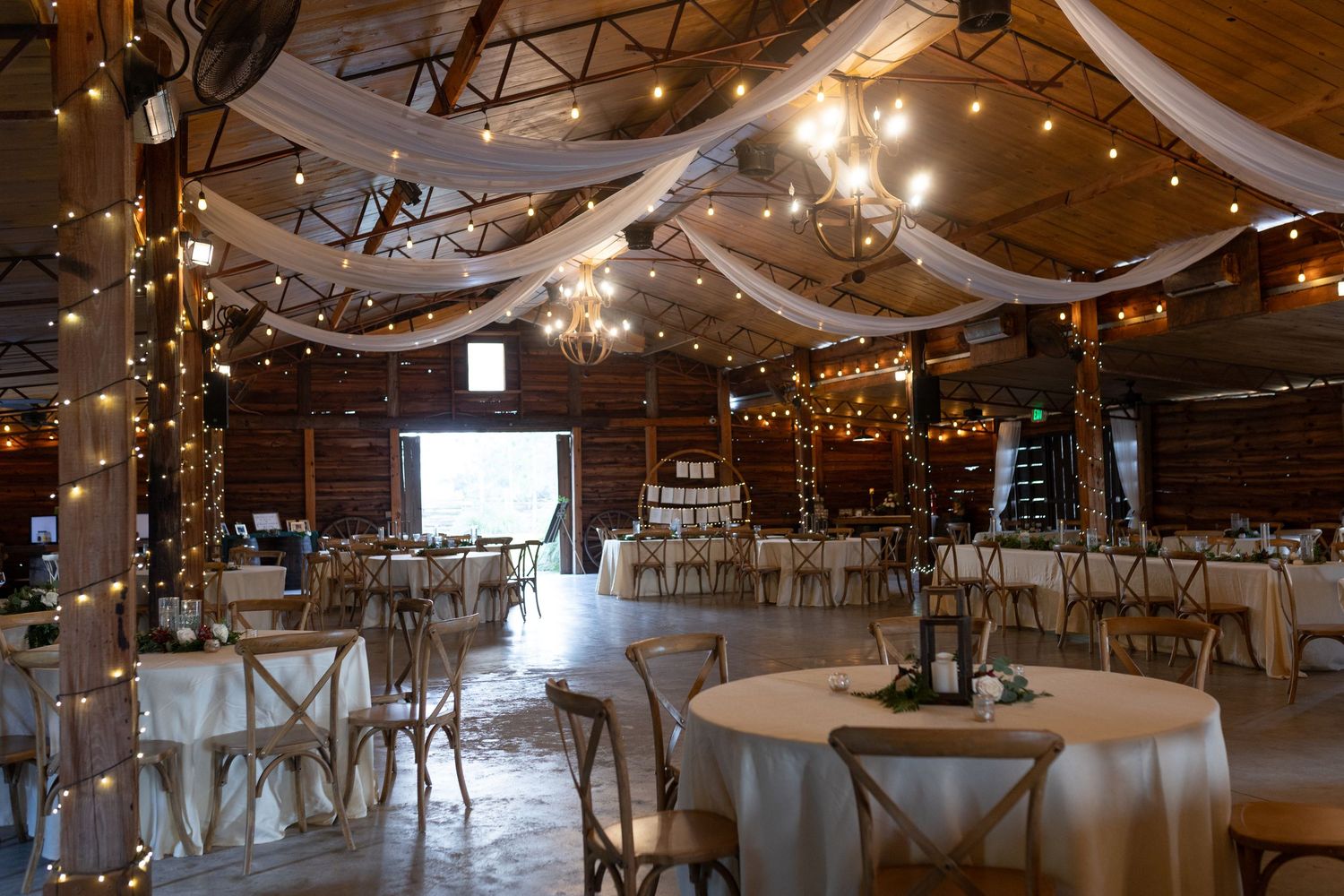 Large rustic wedding reception venue with draped fabric and string lights creating romantic ambiance.