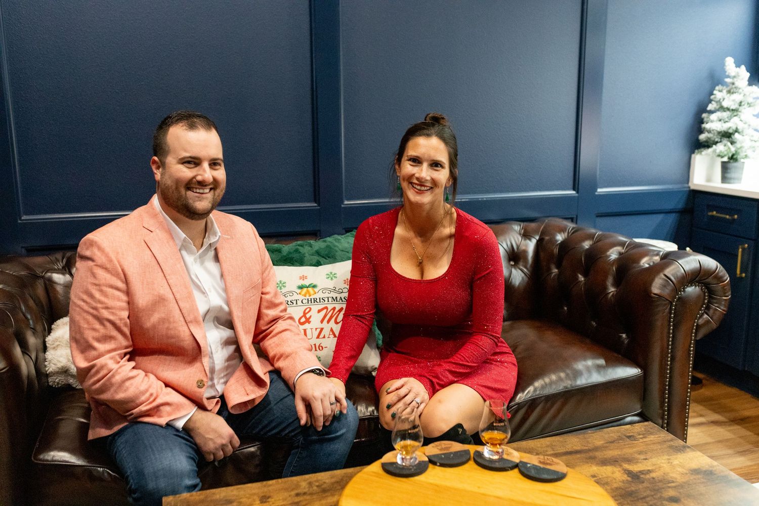 Two people seated on brown leather couch at upscale bar setting.