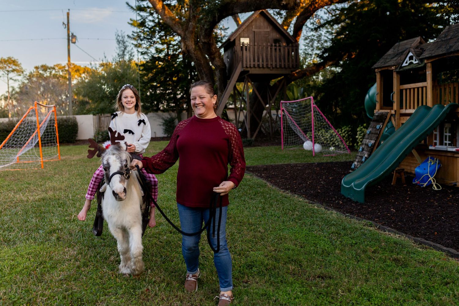 People and dog walking in backyard with playground and autumn trees.