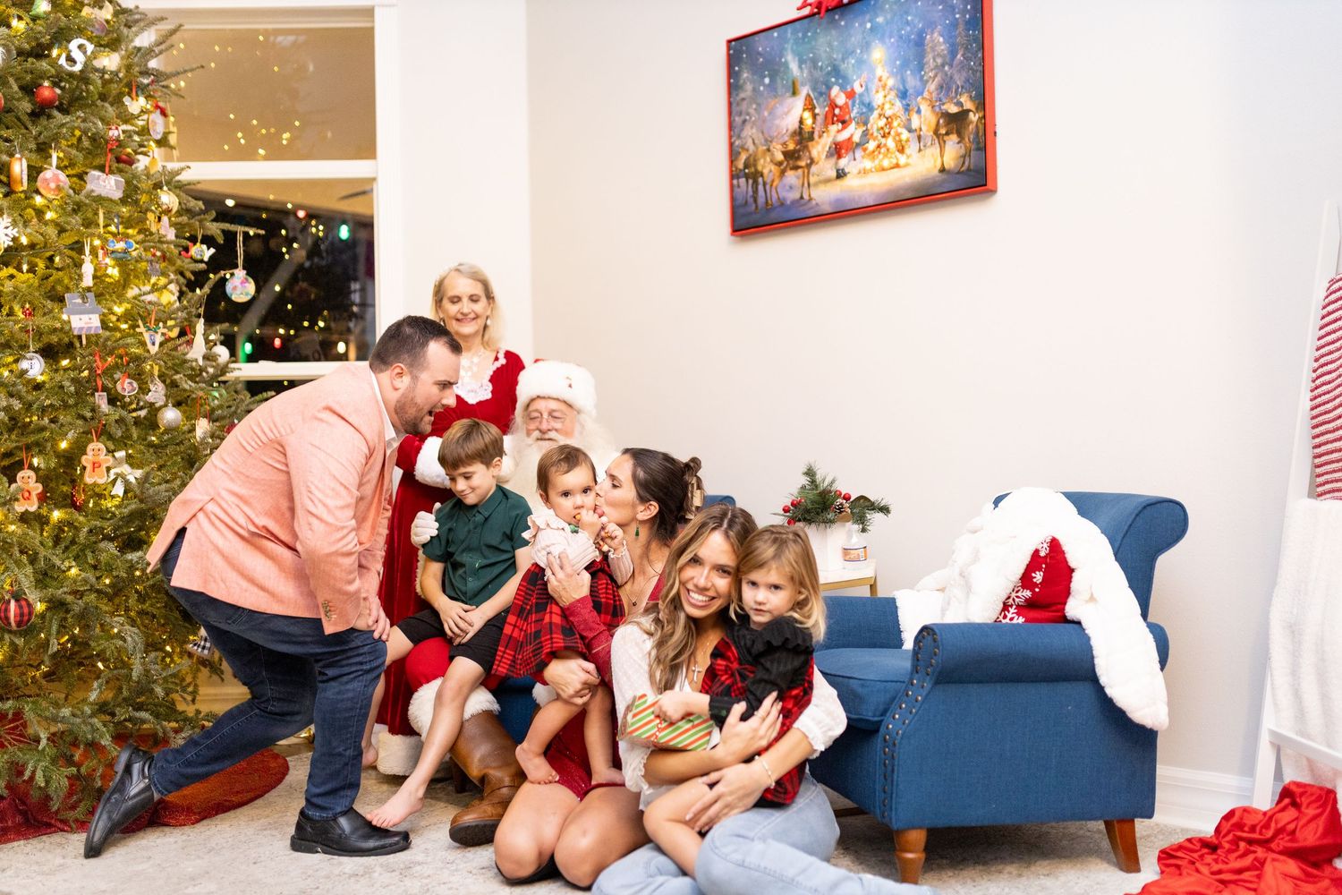 Holiday photo session with family and Santa Claus by decorated Christmas tree and blue couch.