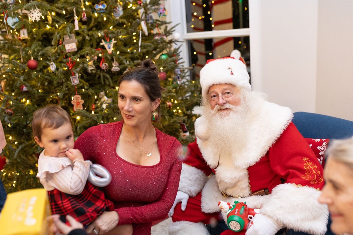A festive Christmas scene with Santa Claus seated by a decorated tree during a holiday photo session.