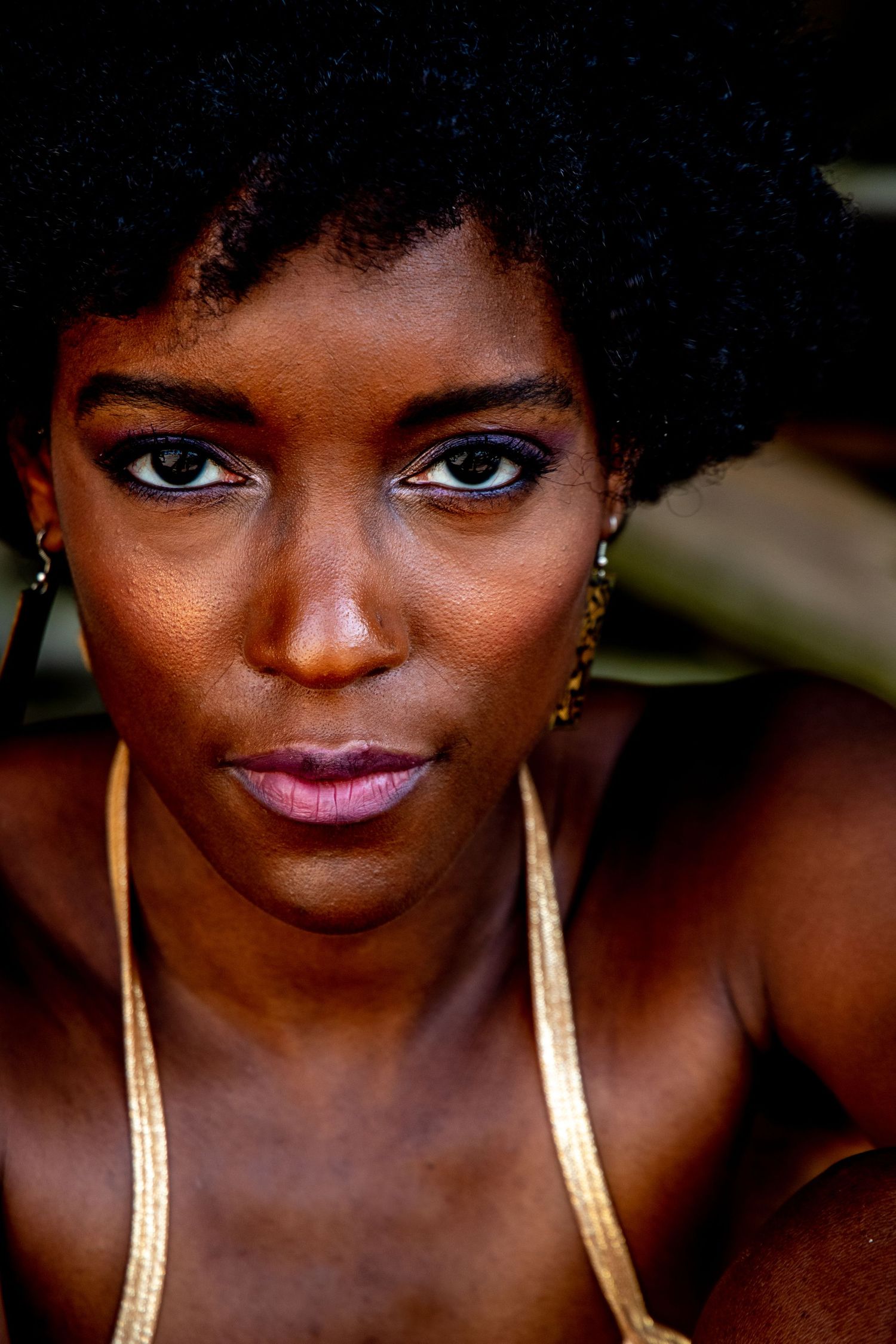 Close-up portrait with gold earrings and vibrant makeup against dark background.