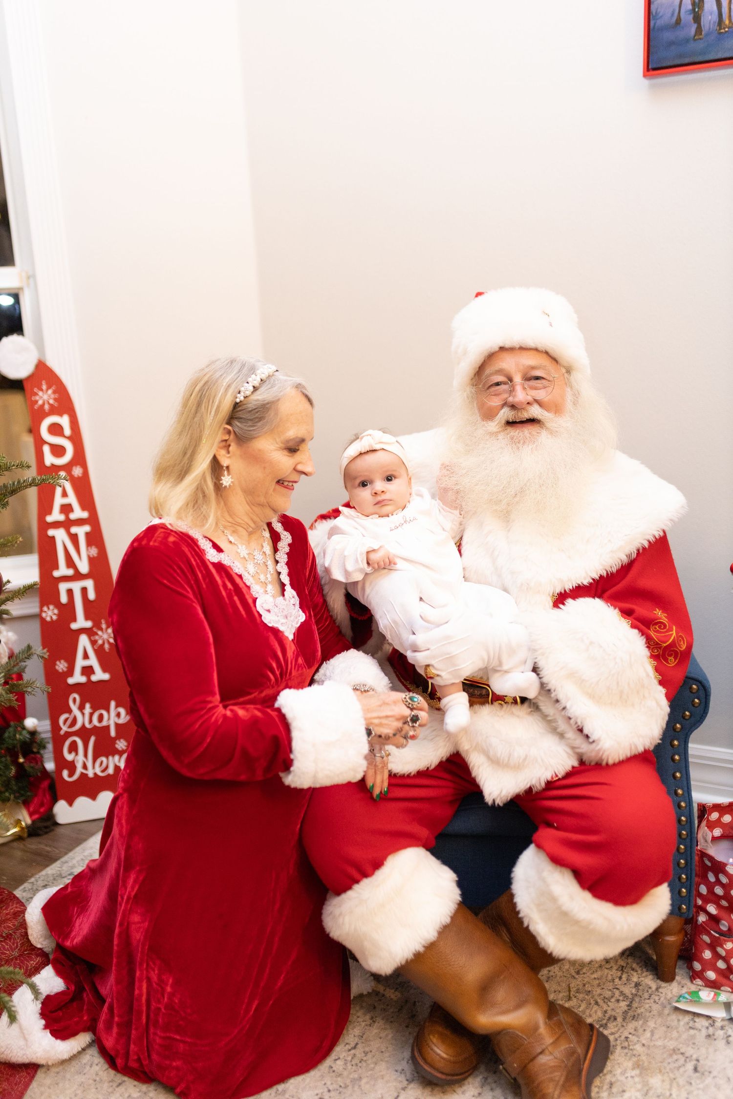 Holiday photo session with festive red decor and Santa signs in the background.