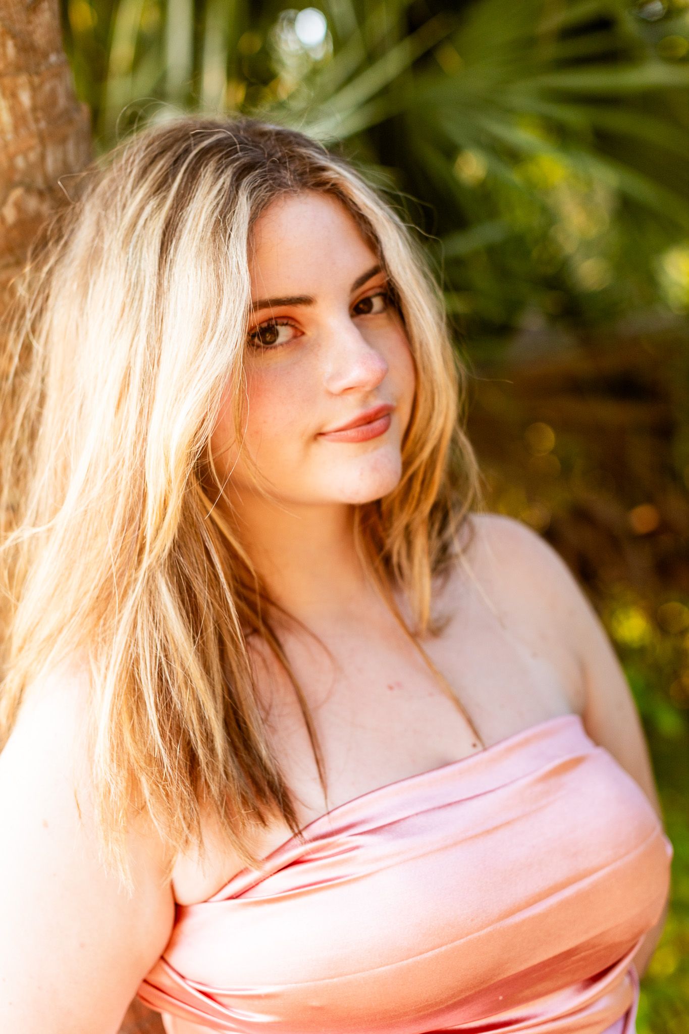 Soft pink dress glowing in dappled sunlight through tropical foliage.