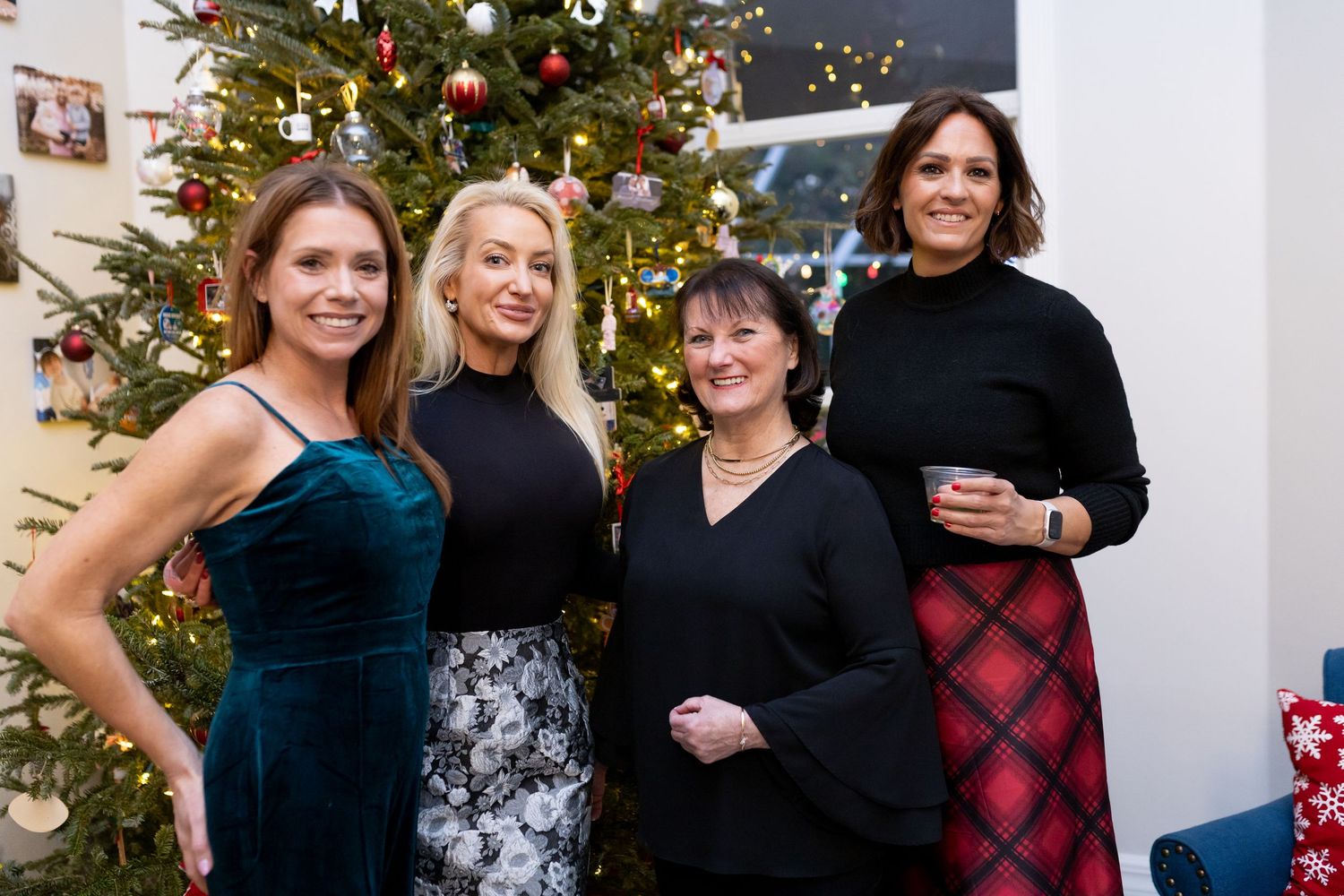 Four people pose together in front of a decorated Christmas tree at a holiday party.