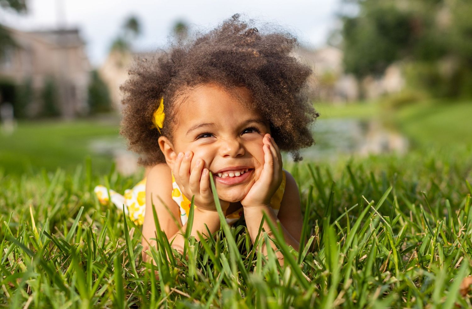 Child poses playfully in green grass during outdoor portrait session.