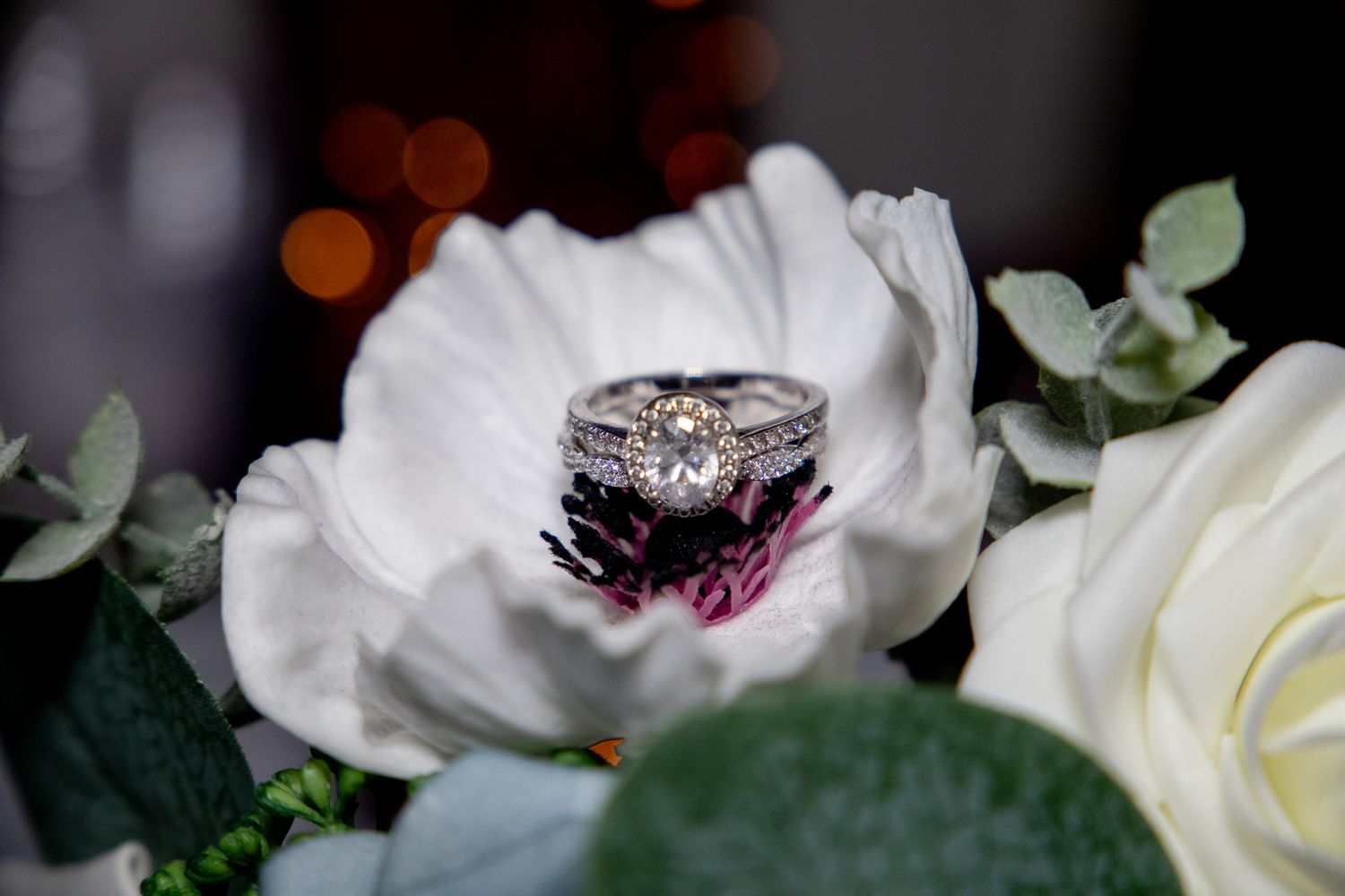 A diamond wedding ring set photographed in a white anemone flower with greenery.