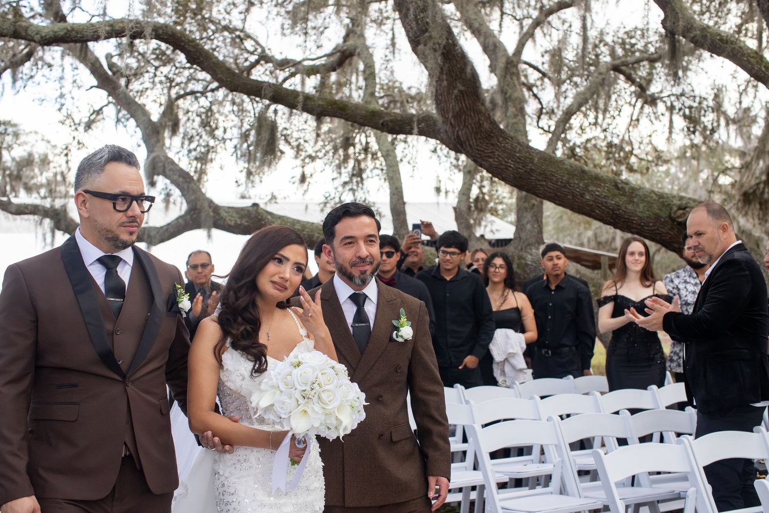 Wedding guests seated in white chairs under oak trees draped with Spanish moss.