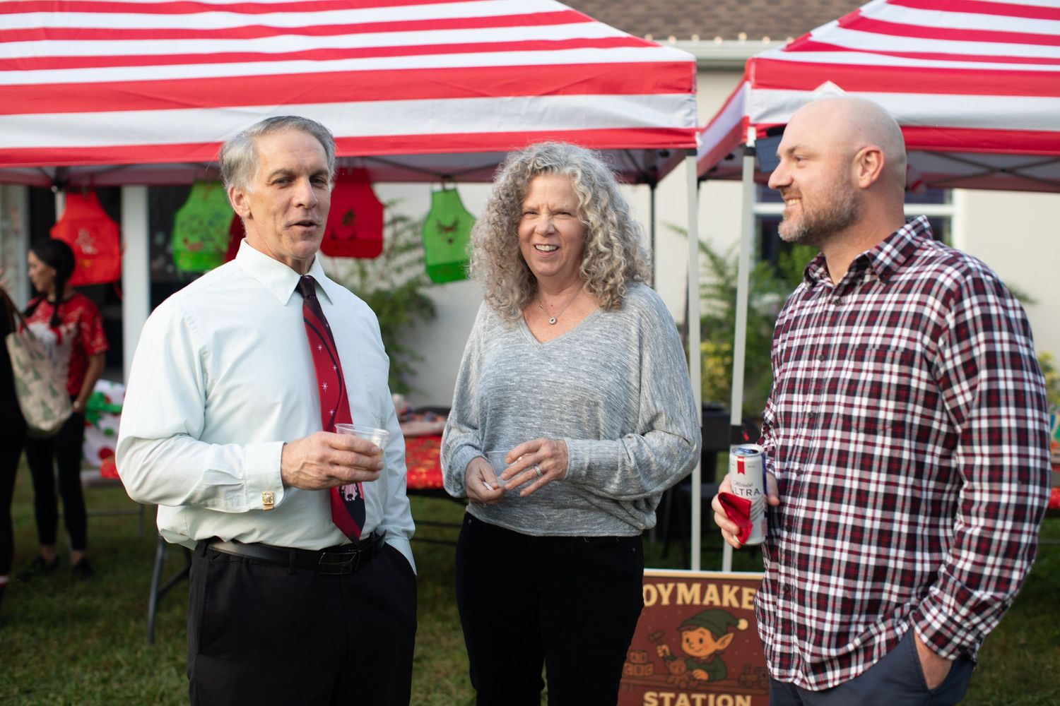 People mingling at an outdoor holiday gathering under a striped tent.