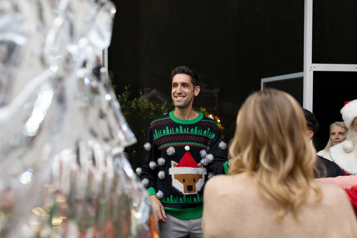 Person wearing green Christmas sweater with reindeer design at holiday gathering.