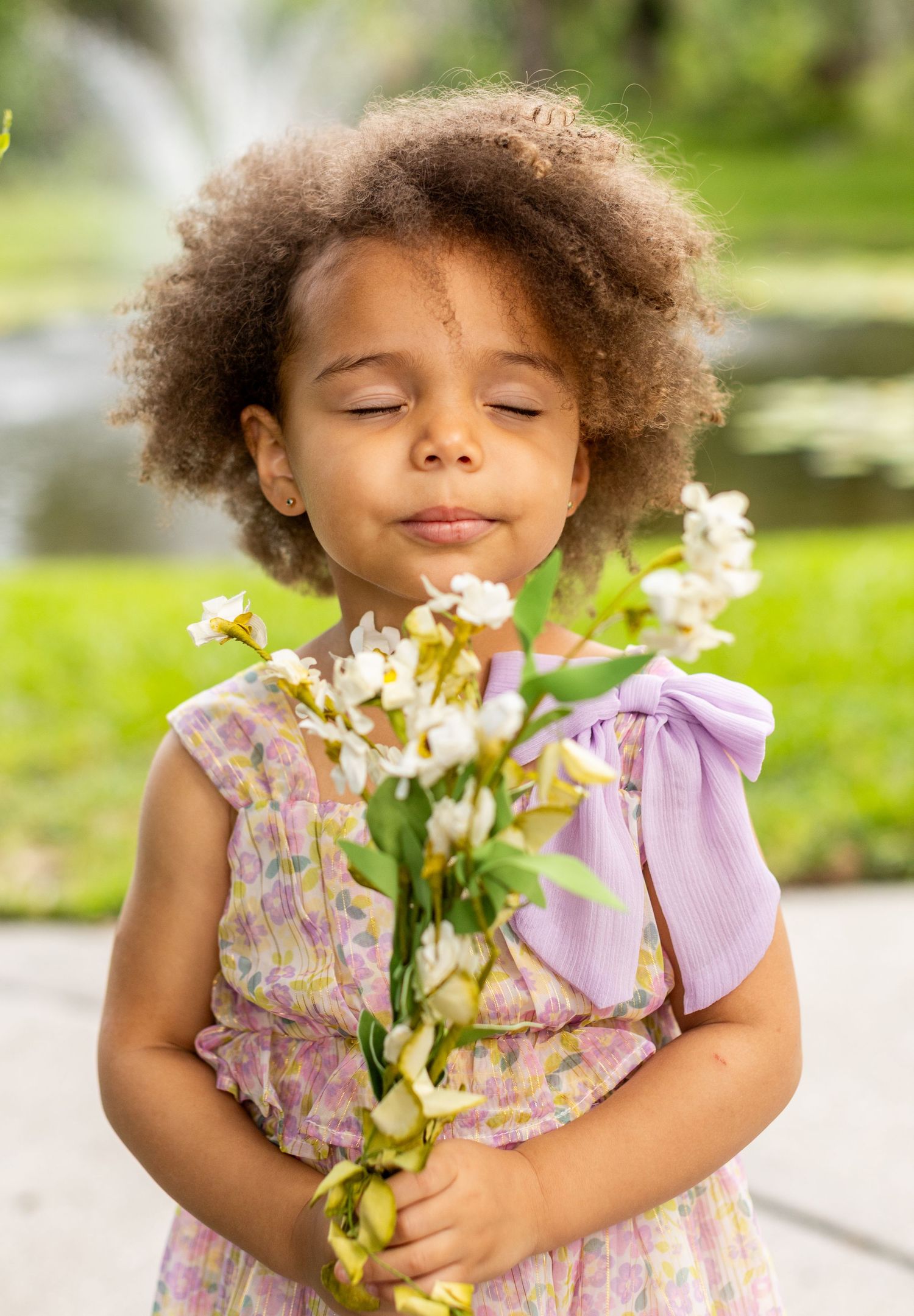 Child in purple floral dress holds white flowers while enjoying springtime garden.