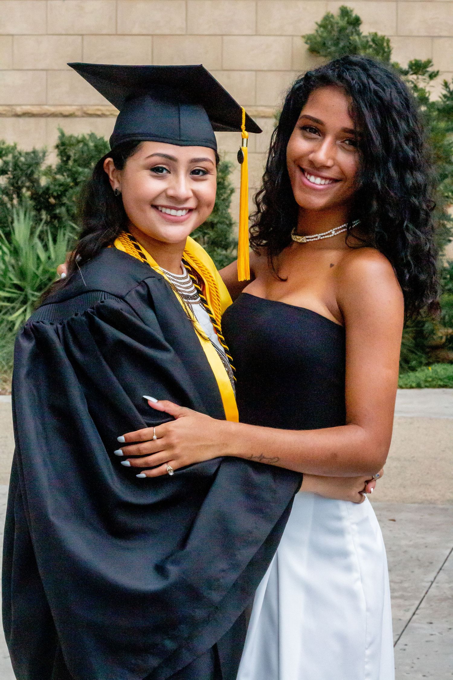 Two people celebrate graduation with hugs and smiles in formal attire.