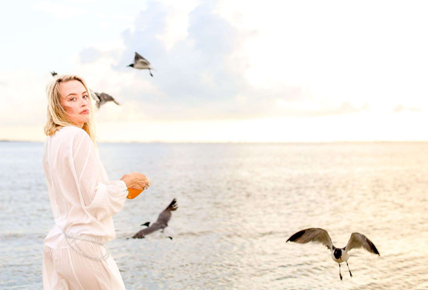 Ethereal beach scene with seabirds circling around figure in white at golden hour.