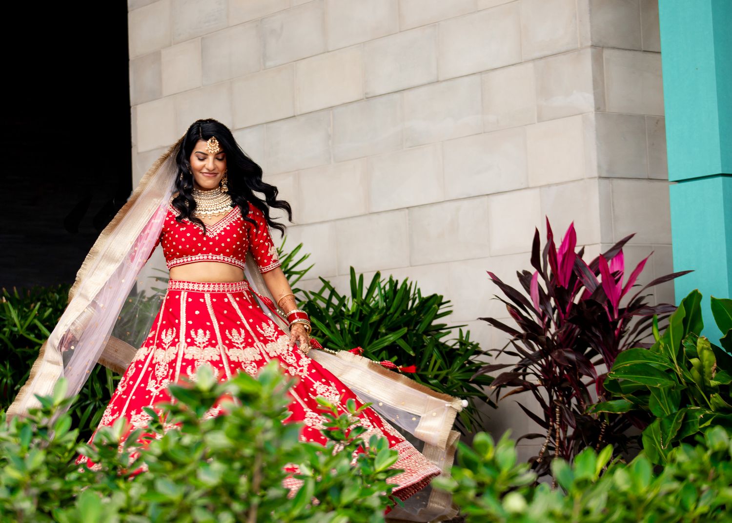 Red and gold lehenga dress photographed in garden setting with tropical plants.