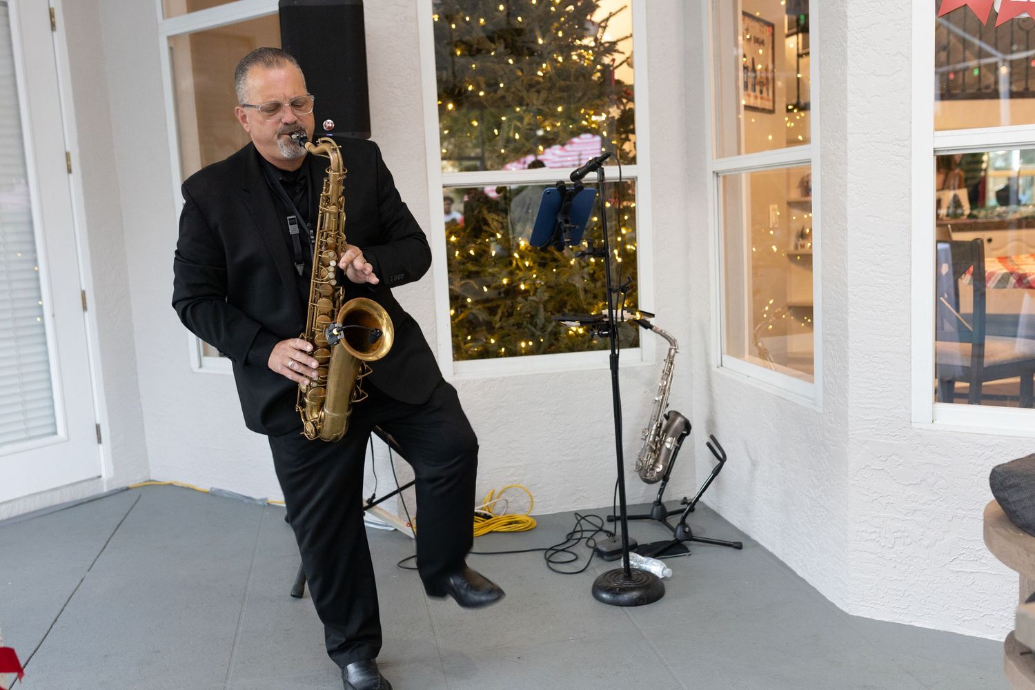 Musician playing saxophone during indoor holiday performance near white columns.