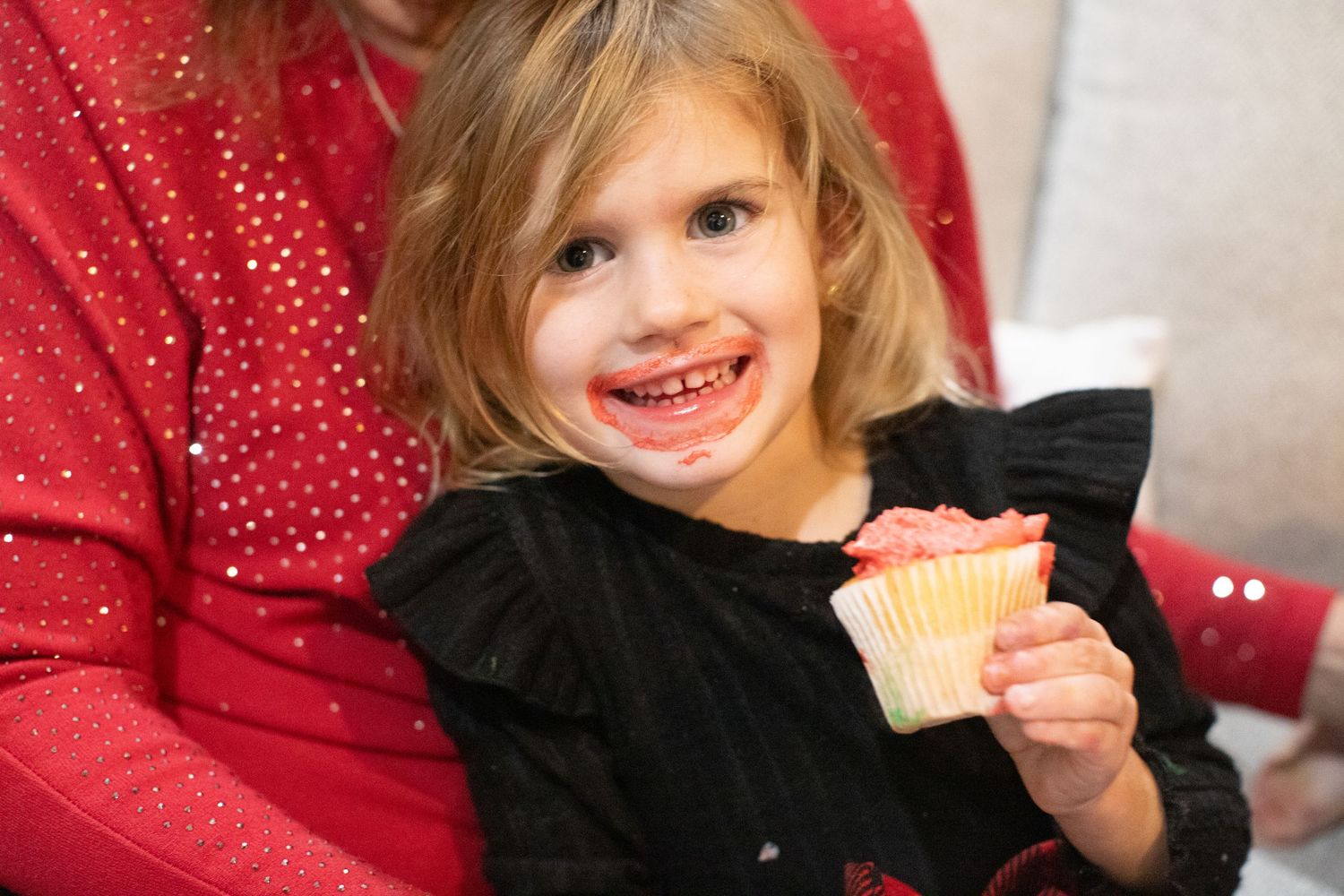 Young child smiles brightly while enjoying holiday festivities in front of Christmas decorations.