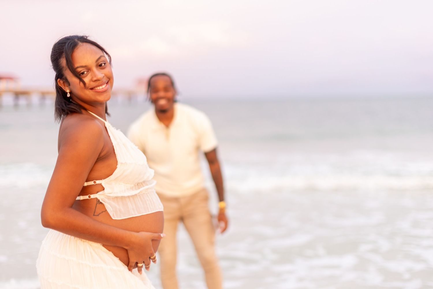 A couple takes maternity photos on the beach at sunset.