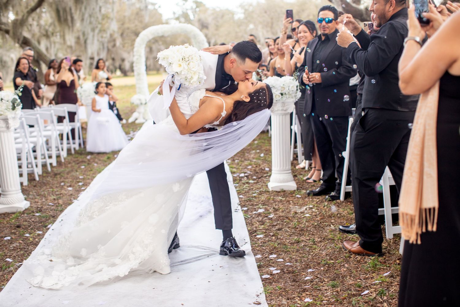 Outdoor wedding celebration with guests gathered among autumn trees.