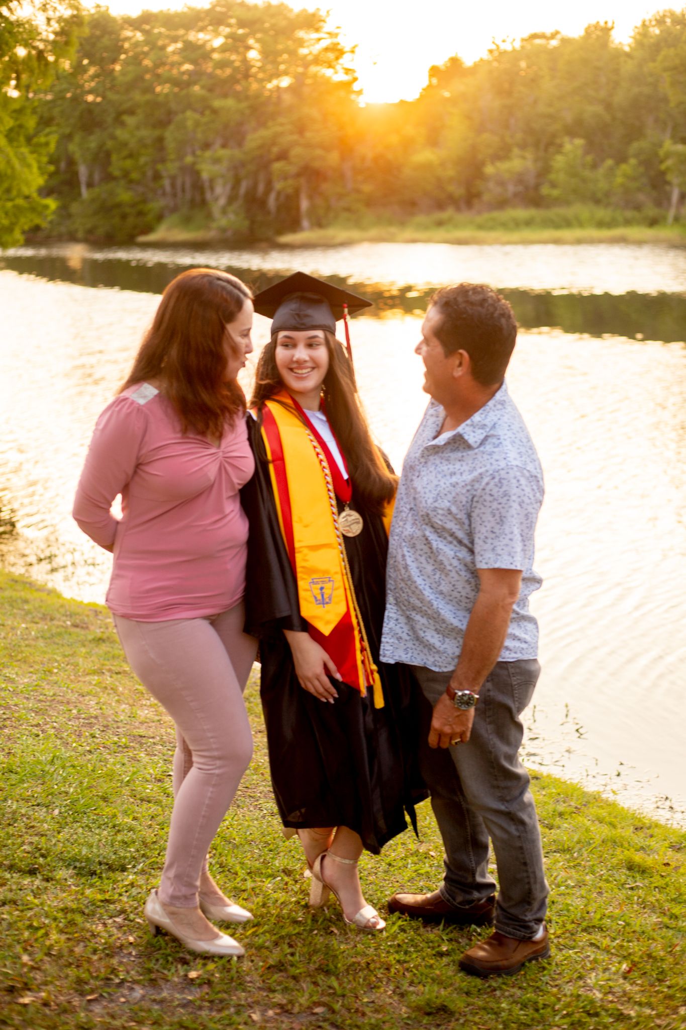 Family members gather around graduate for photos by the lake at sunset.